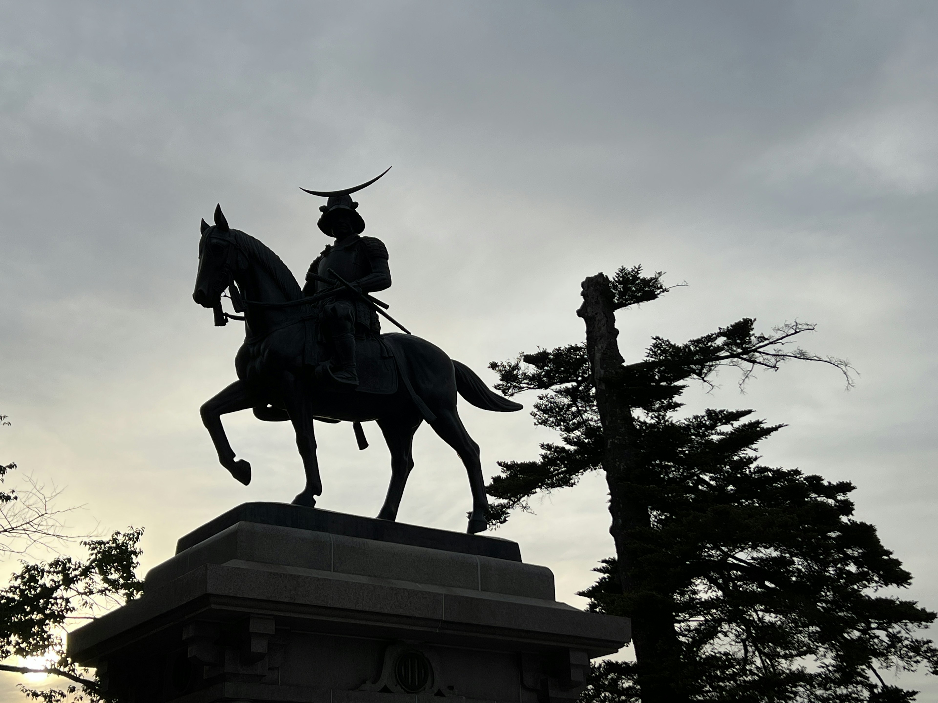 Siluet patung samurai di atas kuda dengan latar belakang langit mendung