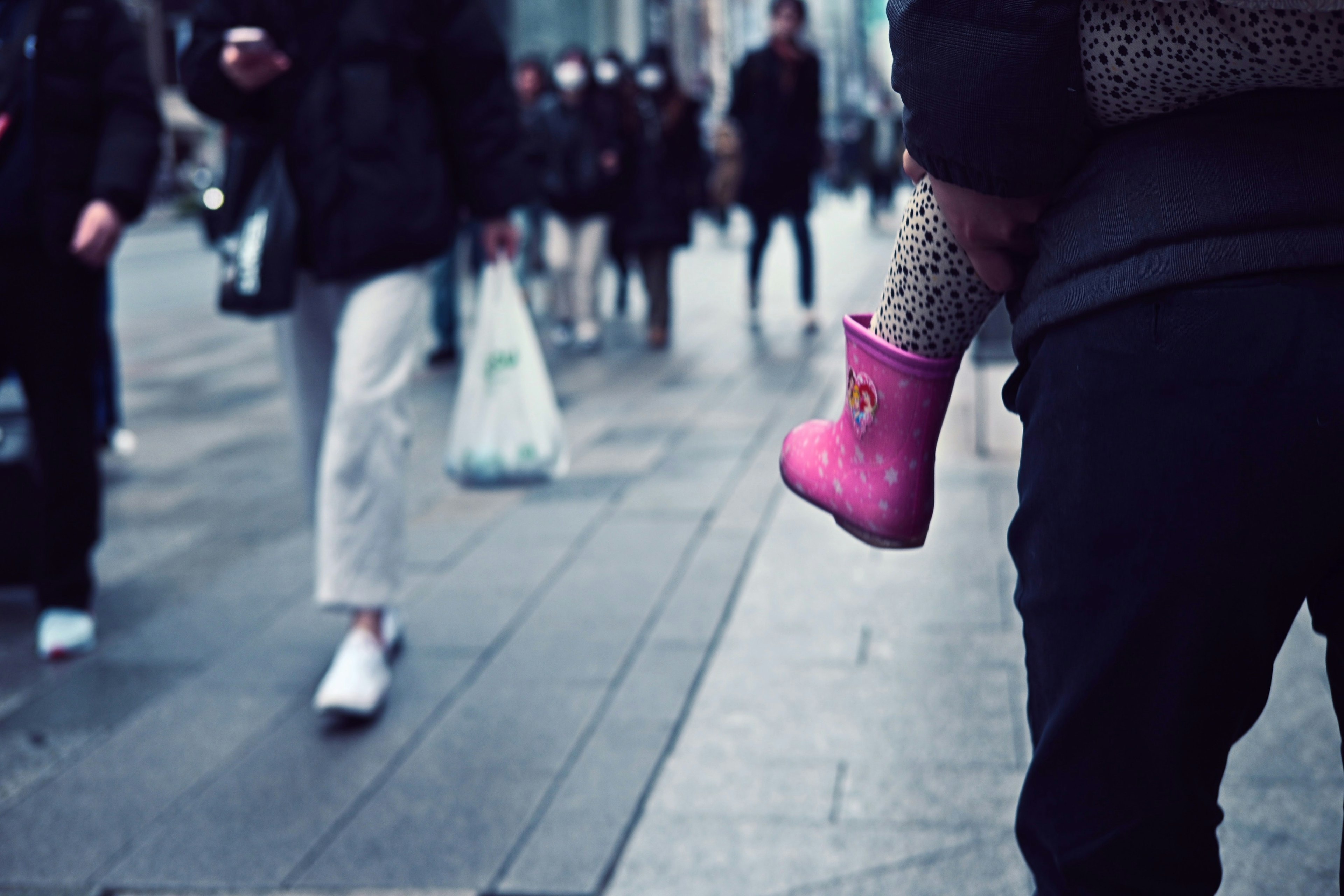 Une scène de rue bondée avec une botte rose d'enfant visible parmi les piétons