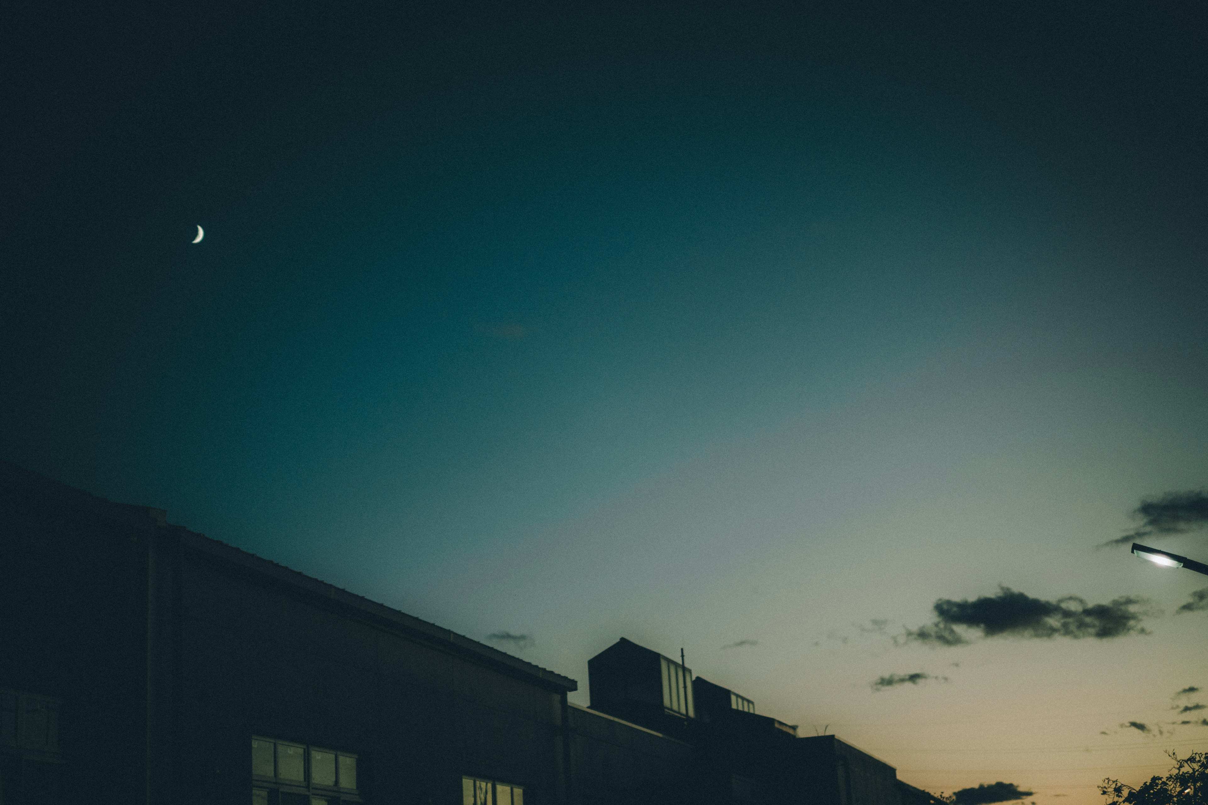 Silhouette of buildings against a twilight sky with a crescent moon