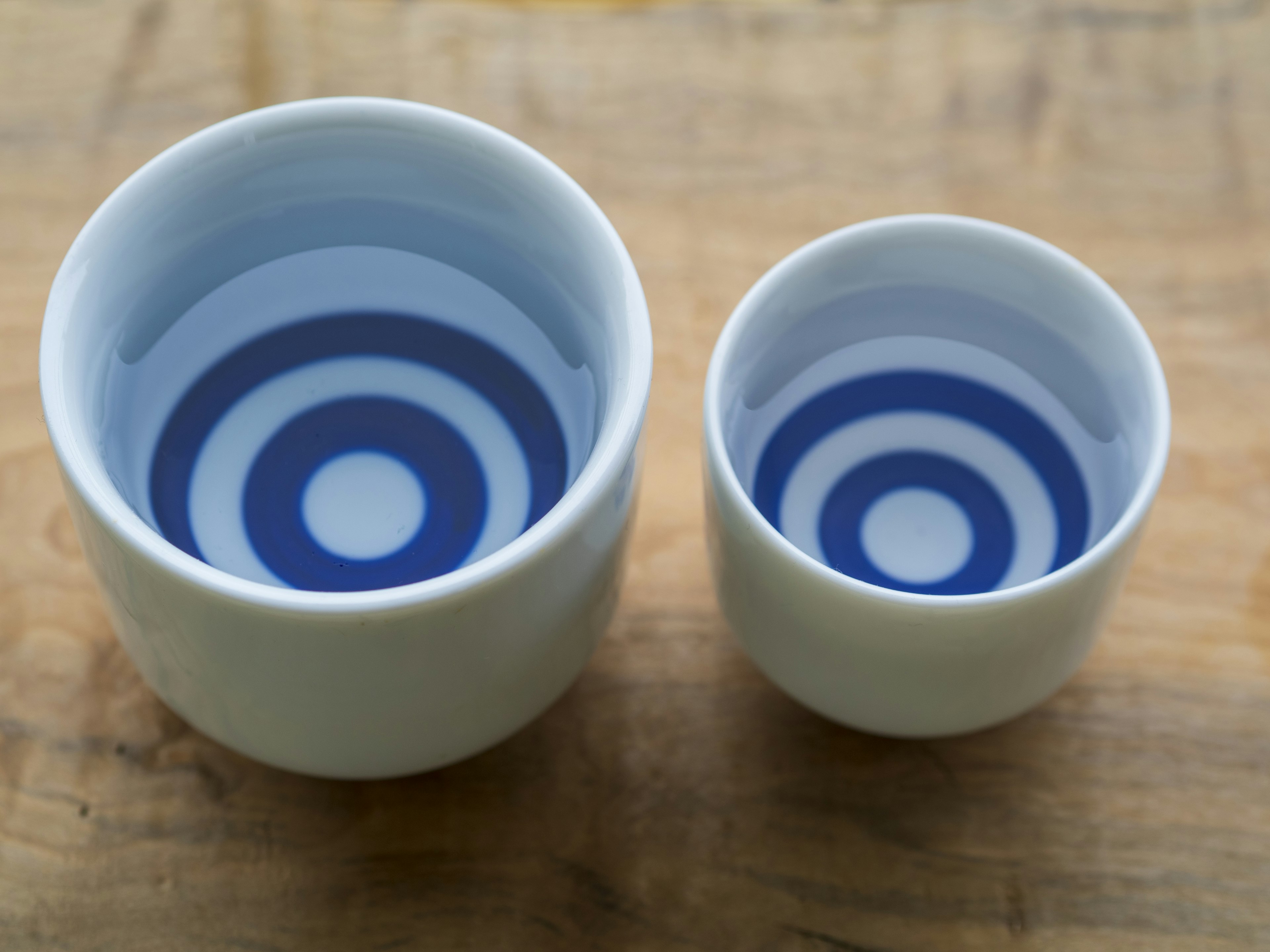 Deux tasses en céramique blanche avec des motifs circulaires bleus à l'intérieur, posées sur une surface en bois