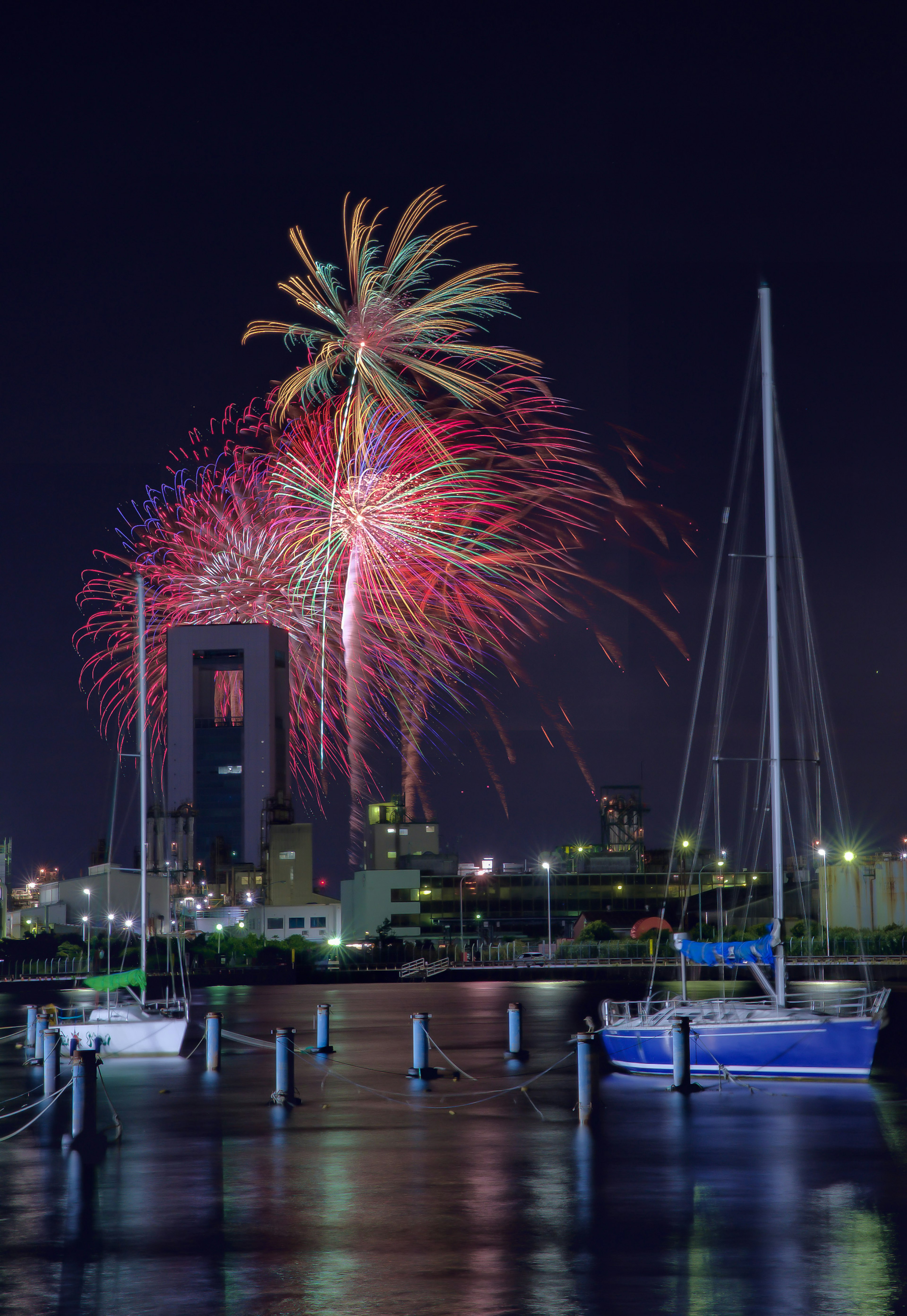 夜空に打ち上げられる花火と静かな港のヨット