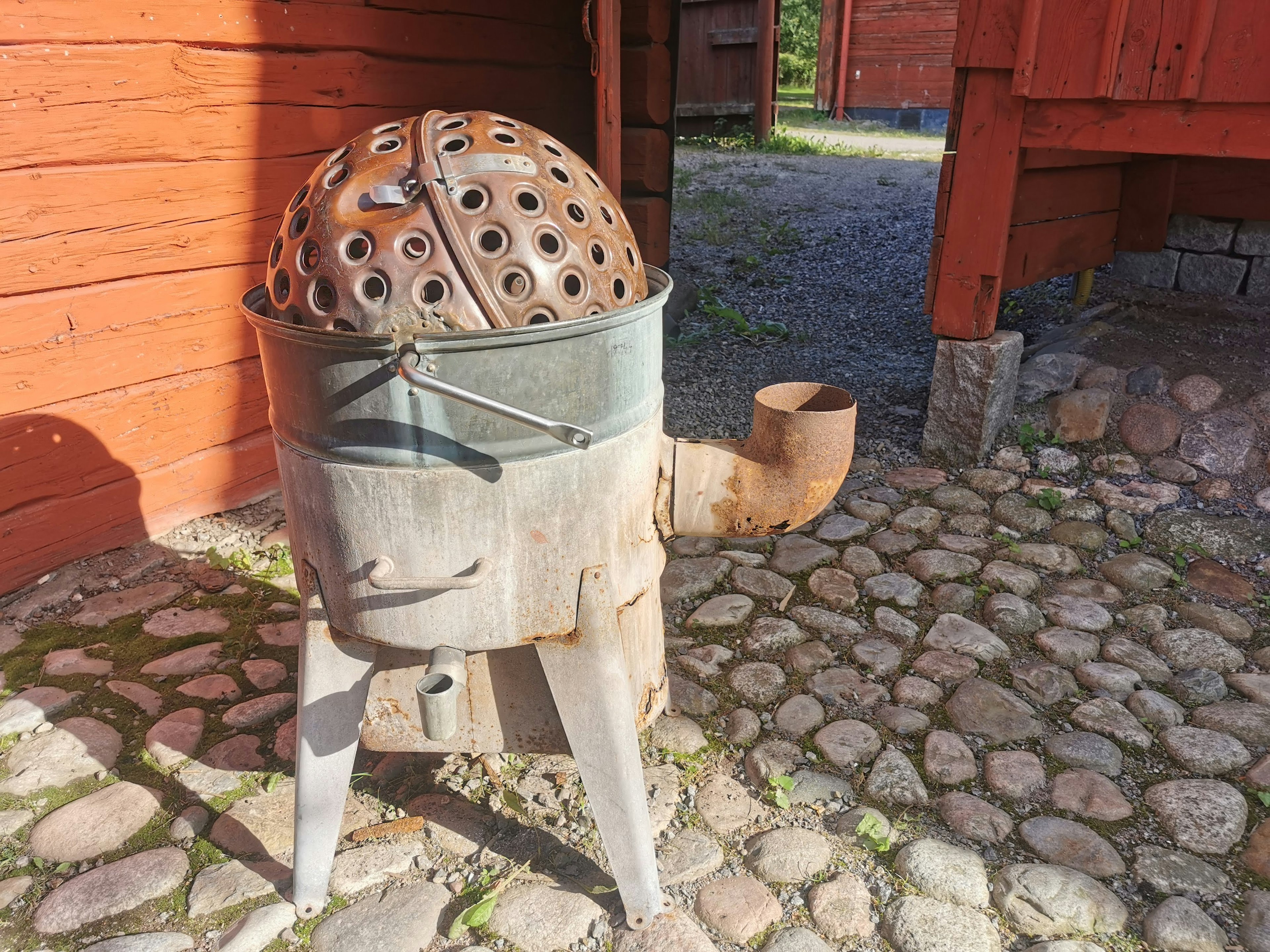 An old metal cooking device on cobblestone ground