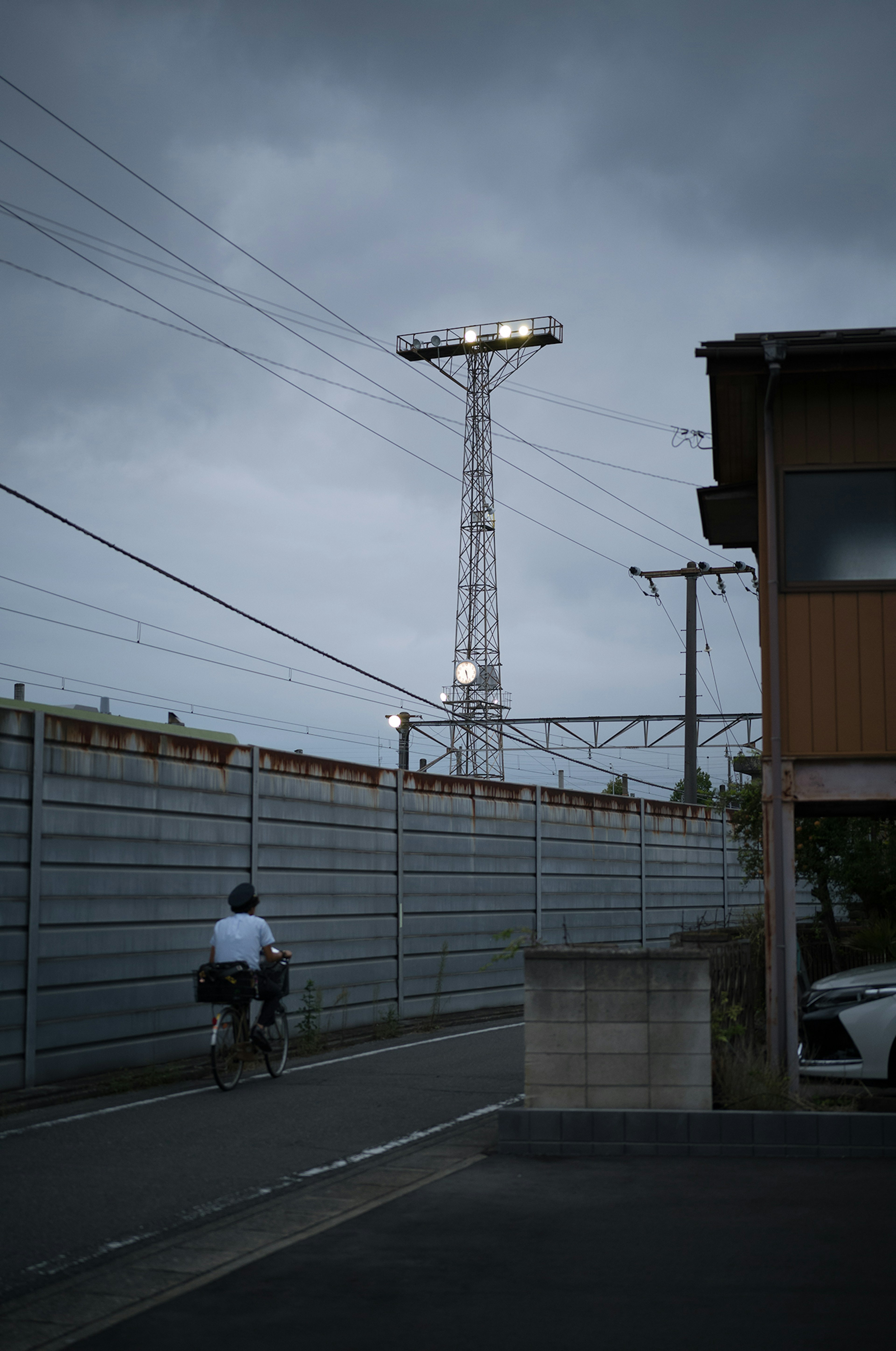 Eine Person auf einem Fahrrad unter dunklen Wolken mit einem hohen Strommast im Hintergrund