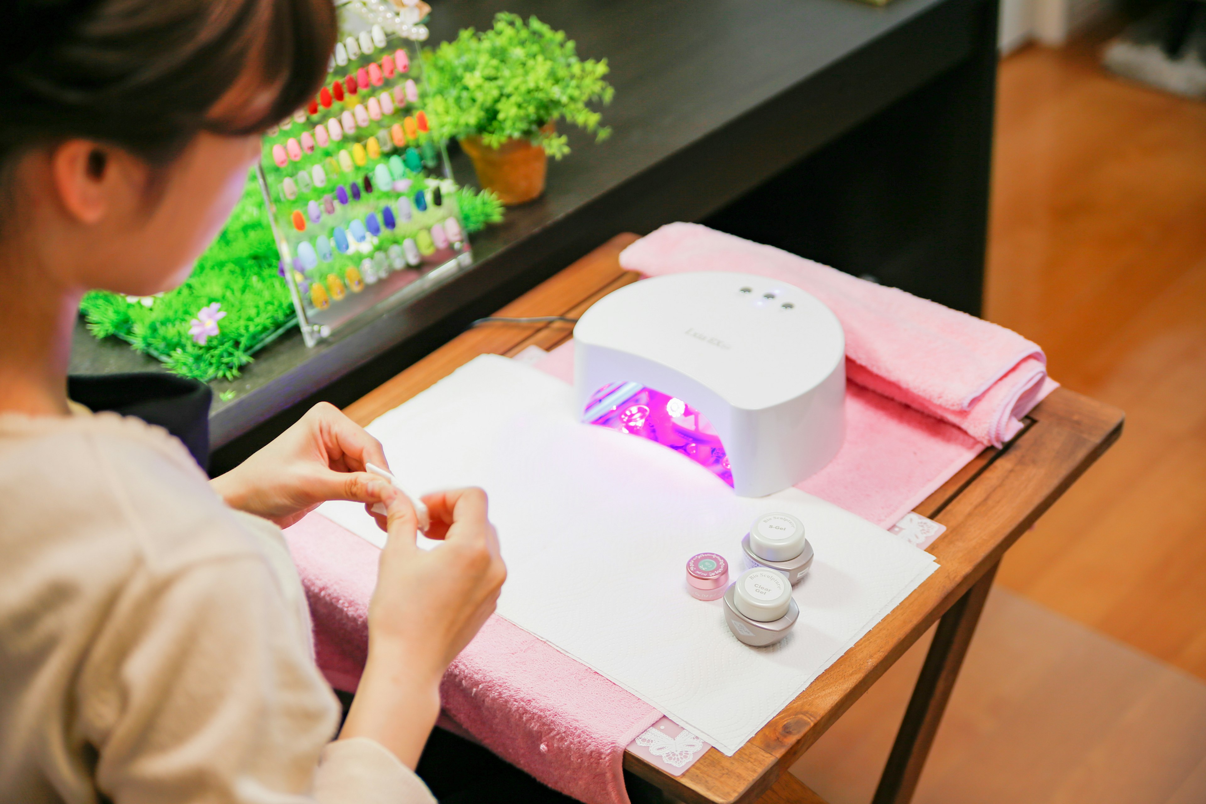 Woman applying gel nails in a nail salon with a purple UV lamp