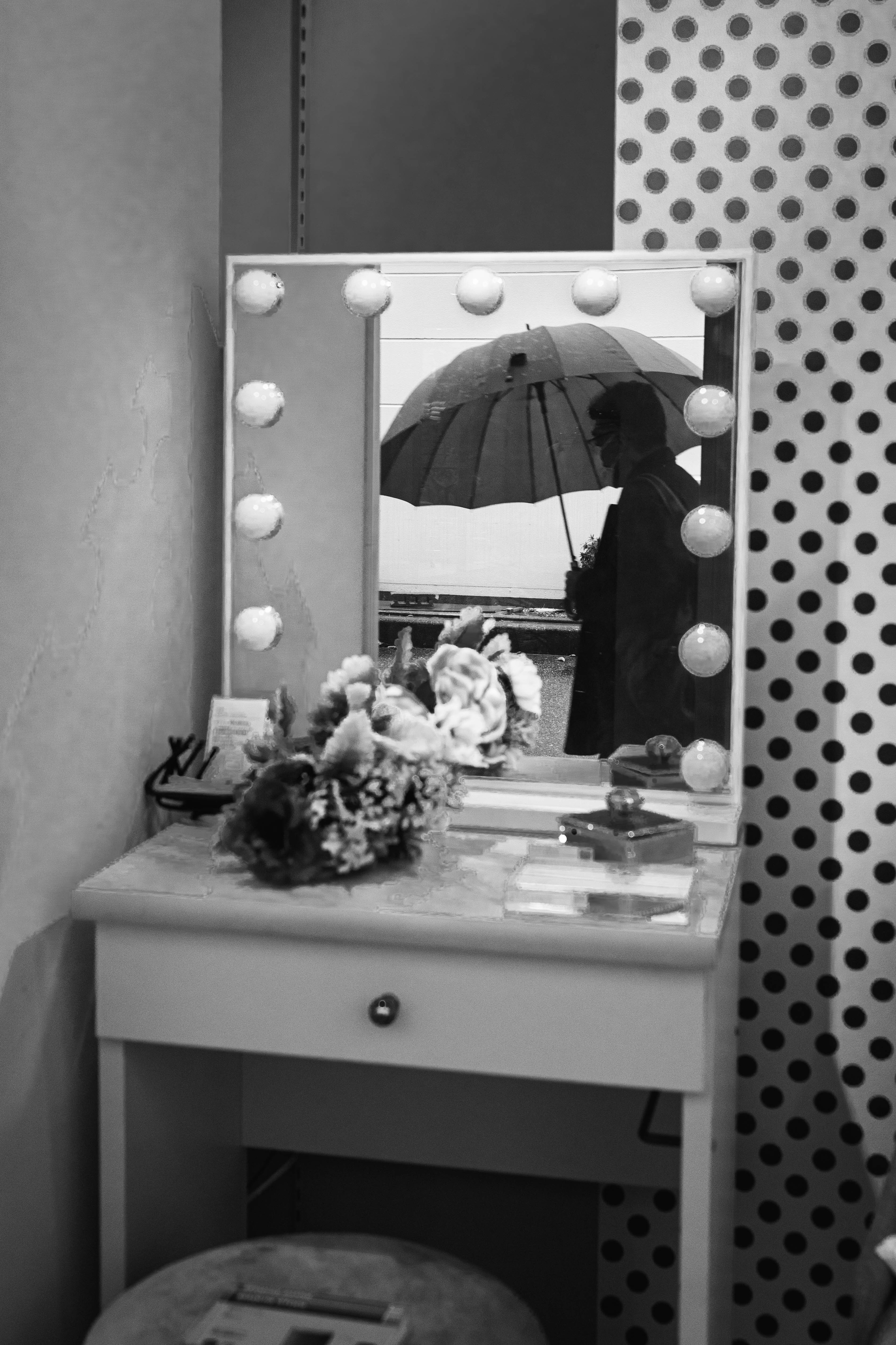 Silhouette of a person holding an umbrella reflected in a vanity mirror with flowers