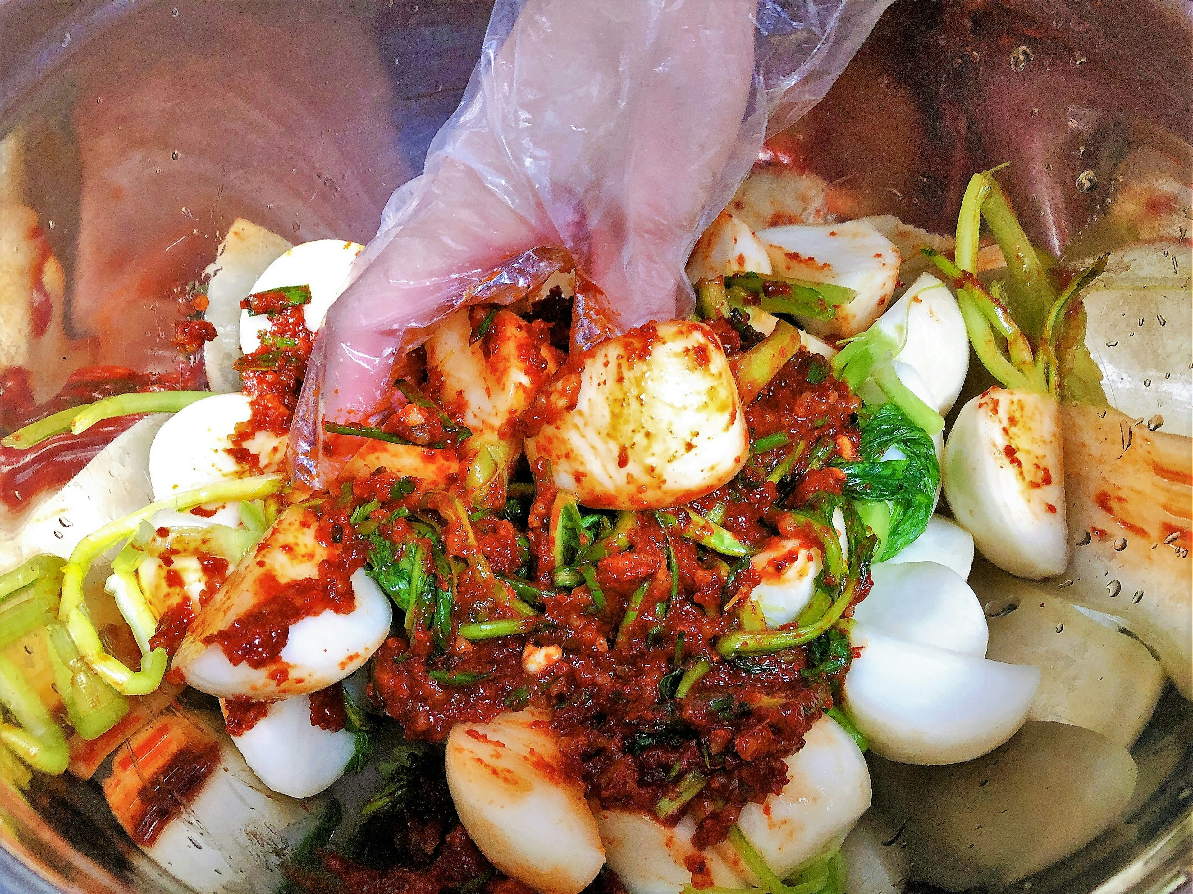 Una mano con guante mezclando verduras y condimentos