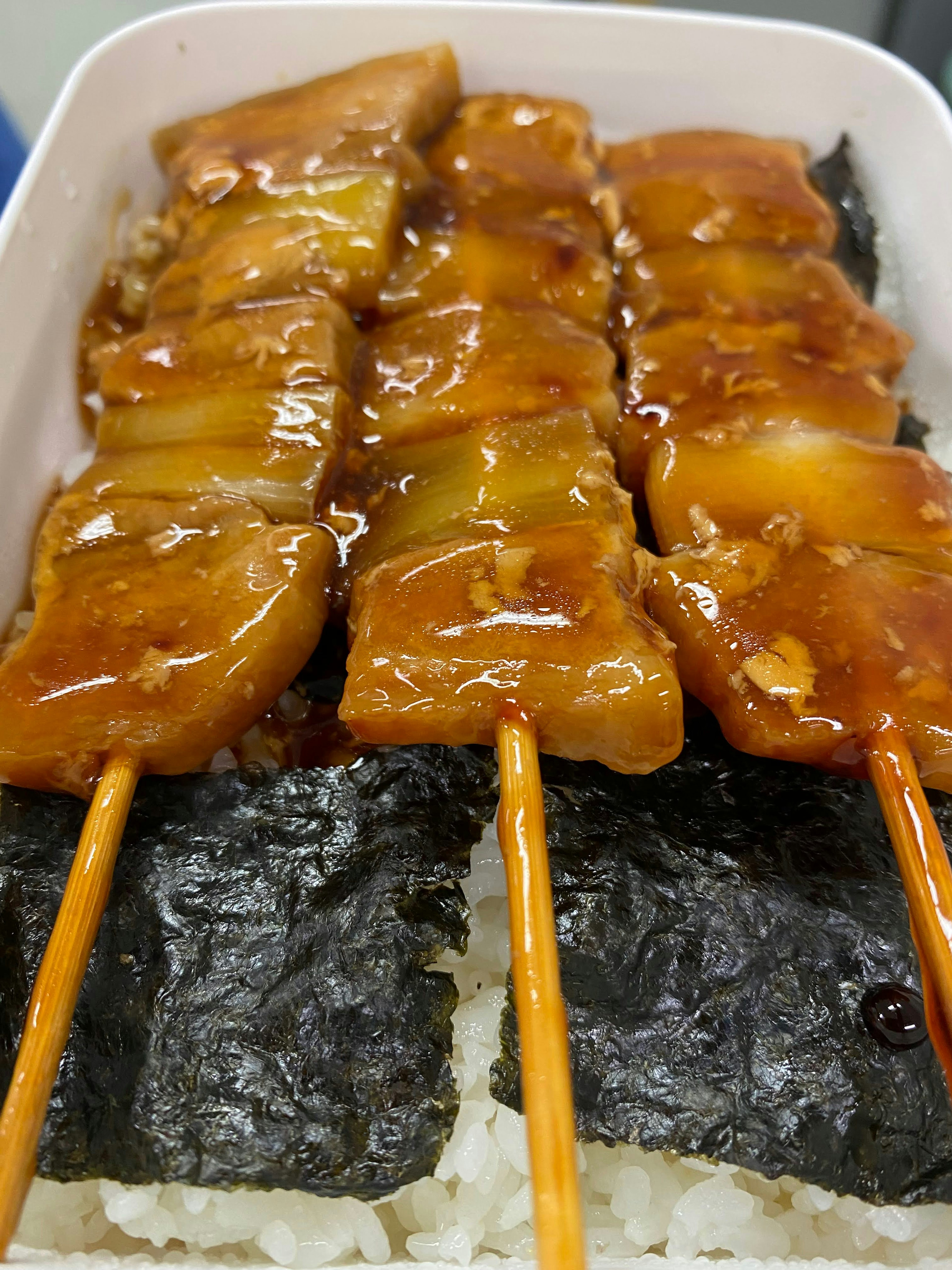 Grilled chicken skewers with sauce served over rice and seaweed