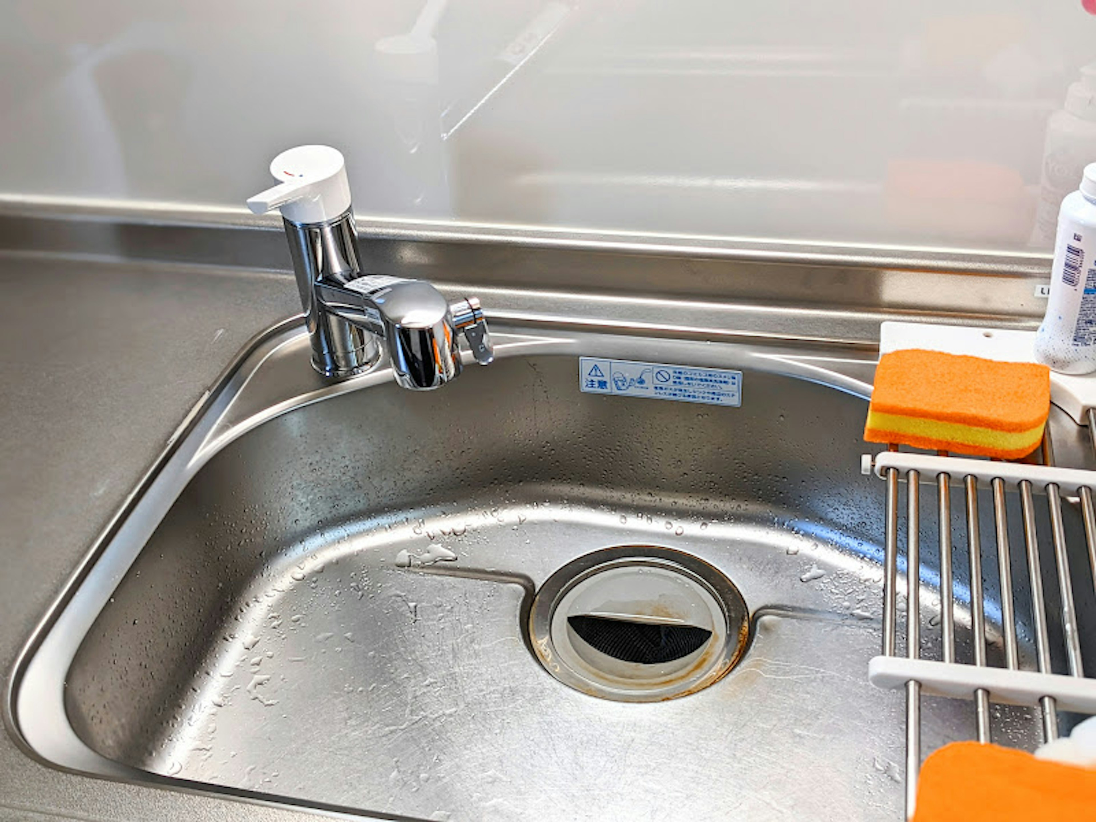 Kitchen sink with faucet featuring sponges and drying rack