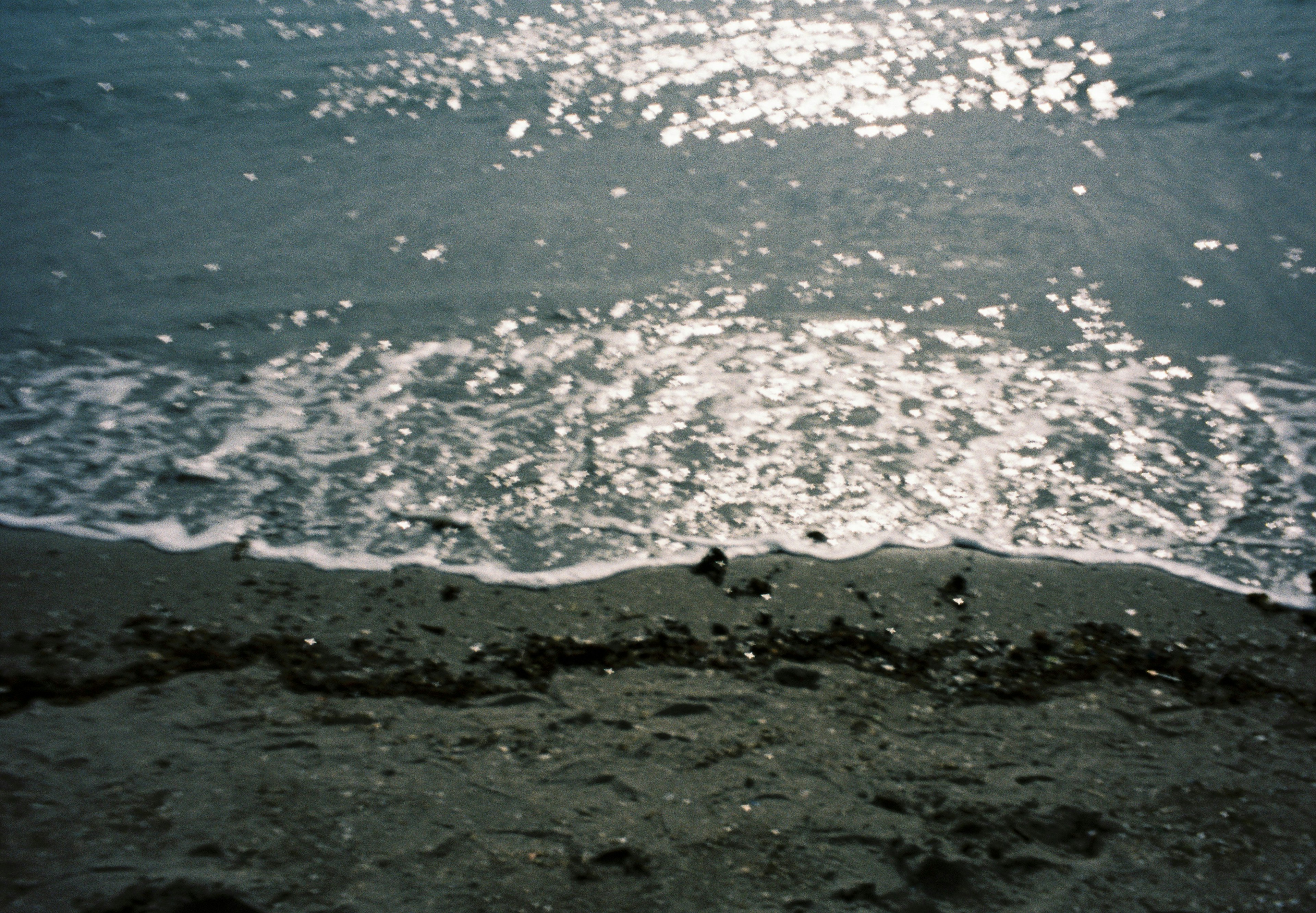 Riva con onde che si infrangono e riflesso del sole sull'acqua