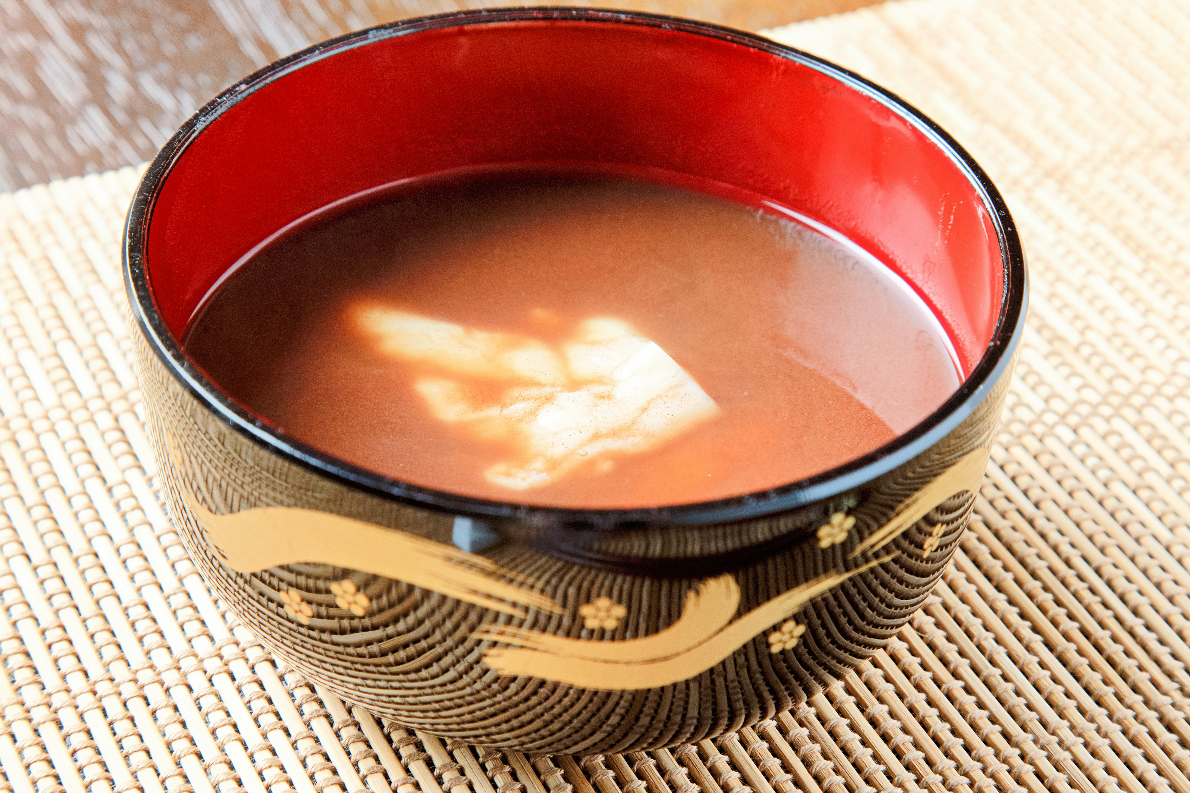 Black bowl with red interior and golden patterns containing soup