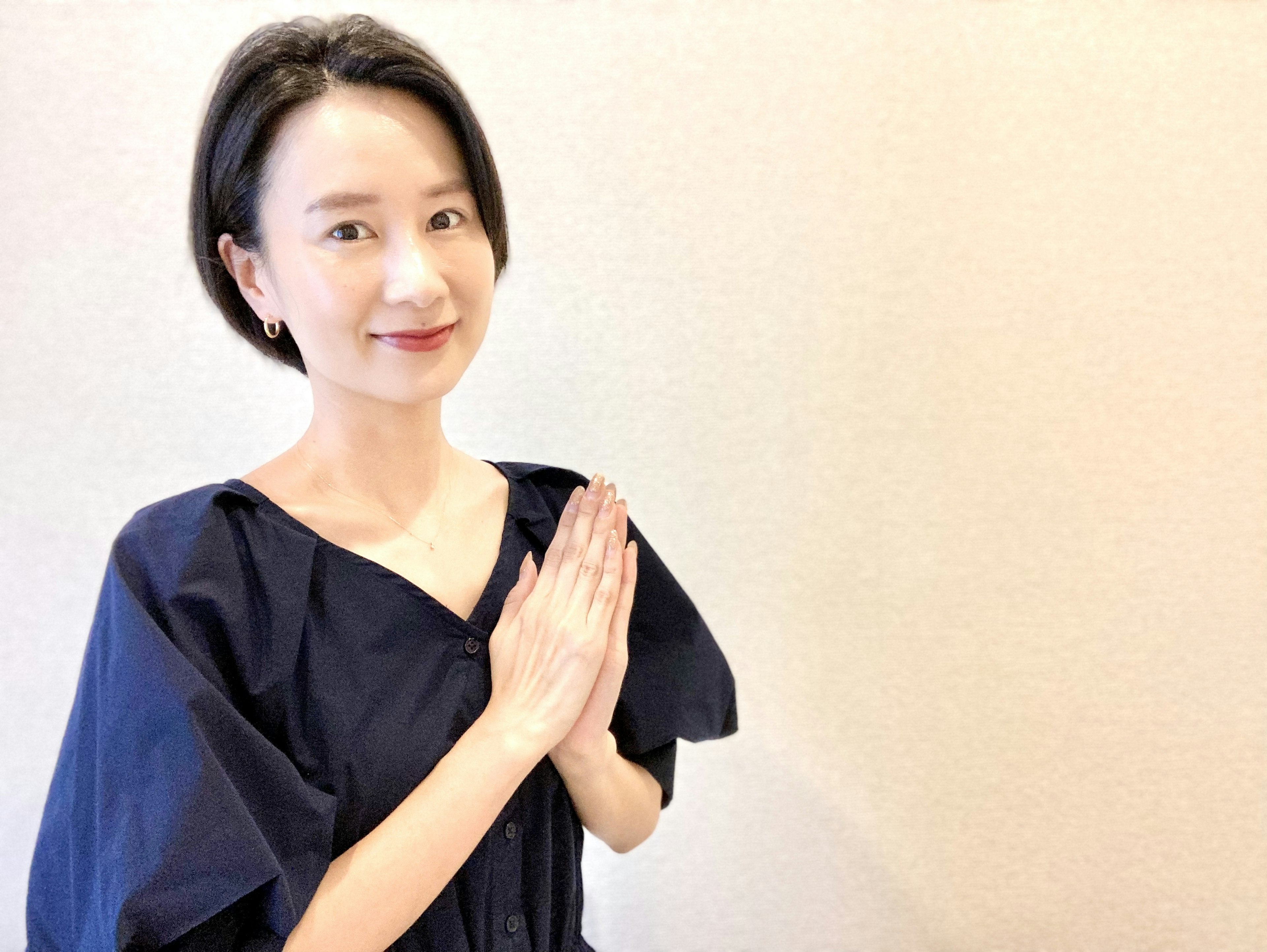 A woman in a black outfit smiling with her hands together