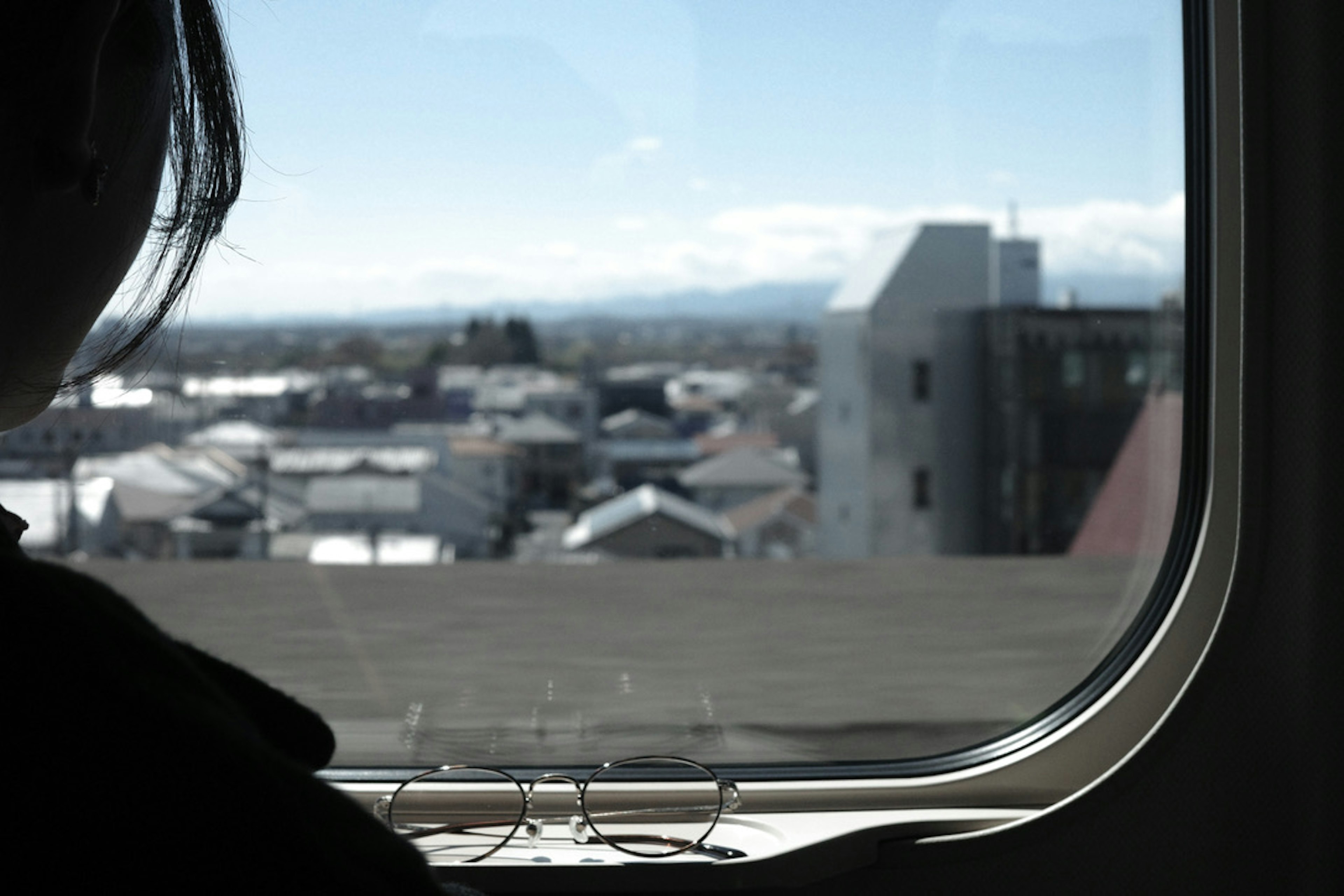 Silhouette of a person gazing out a train window at a cityscape