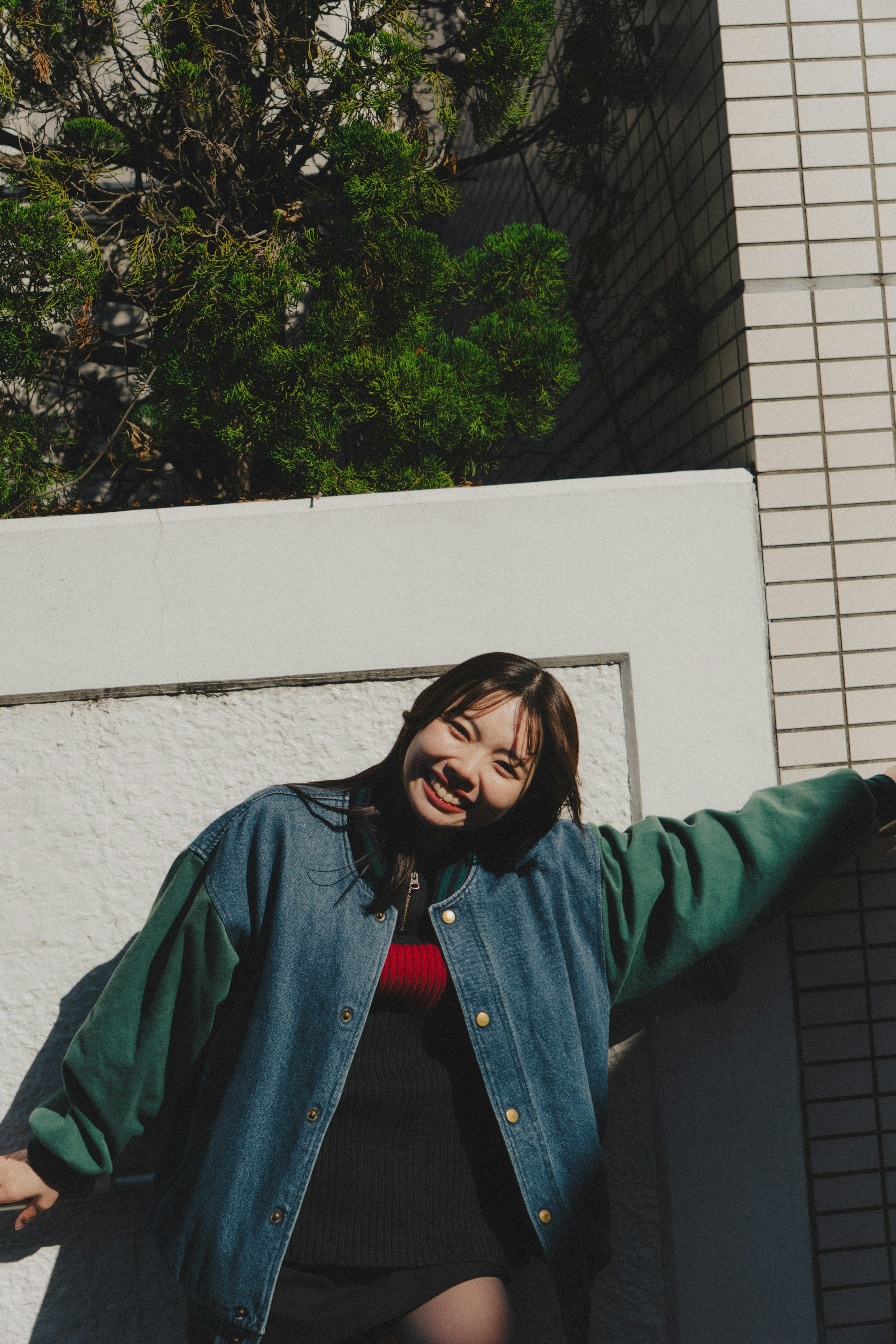 A smiling woman wearing a green jacket leaning against a wall