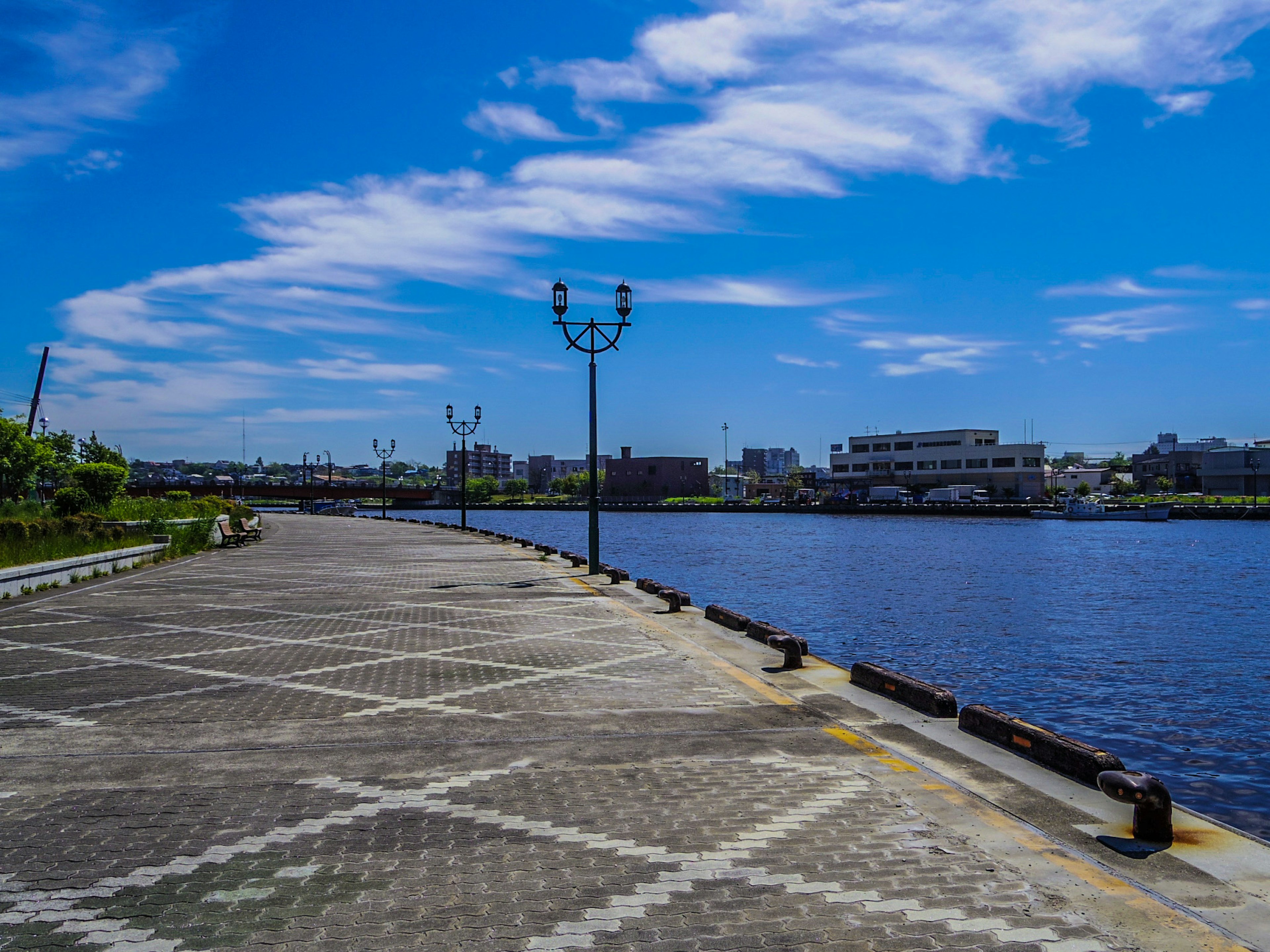 Promenade pavée au bord de la rivière sous un ciel bleu avec des nuages épars