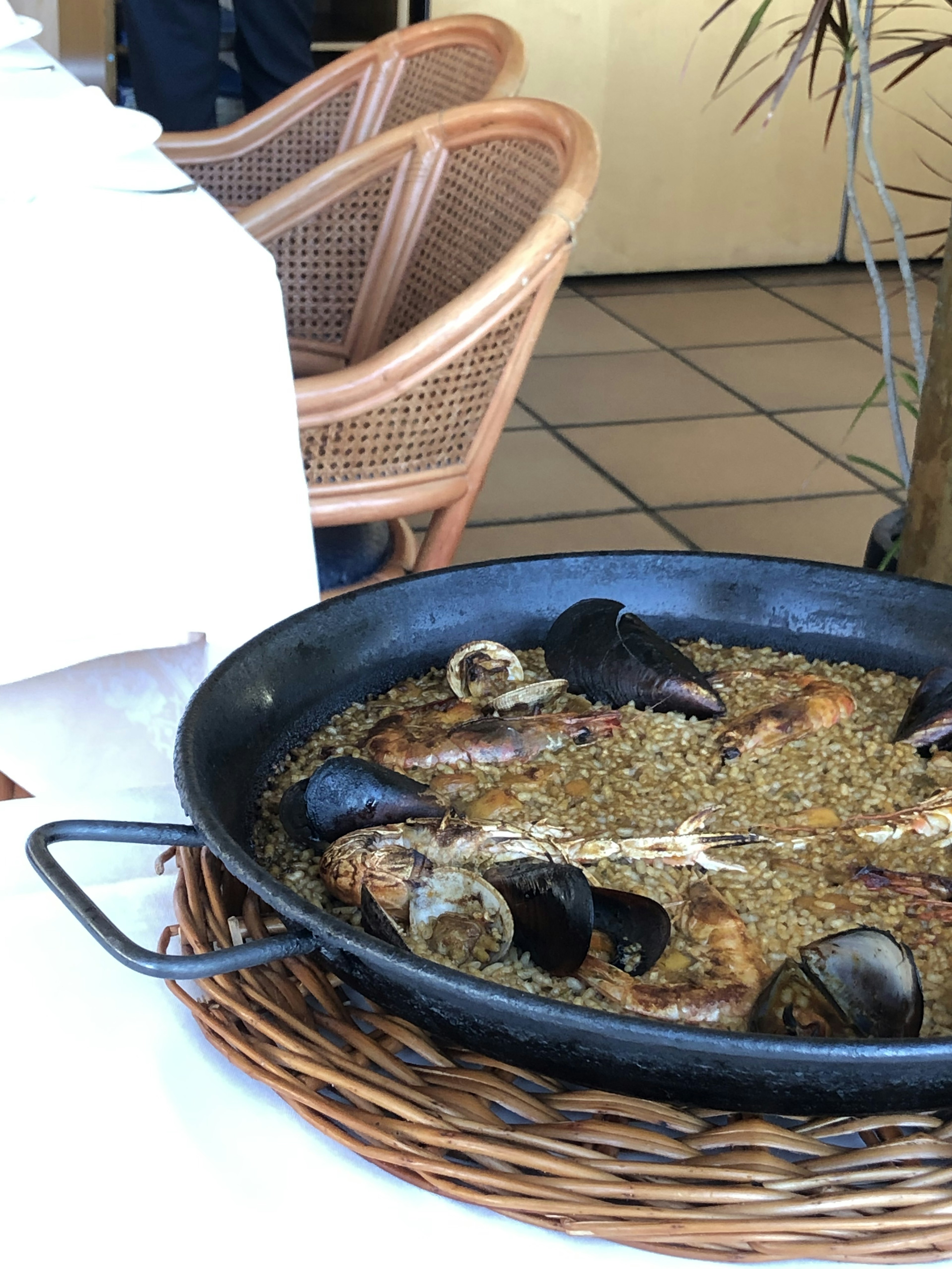 Paella seafood disajikan dalam panci hitam di atas keranjang rotan