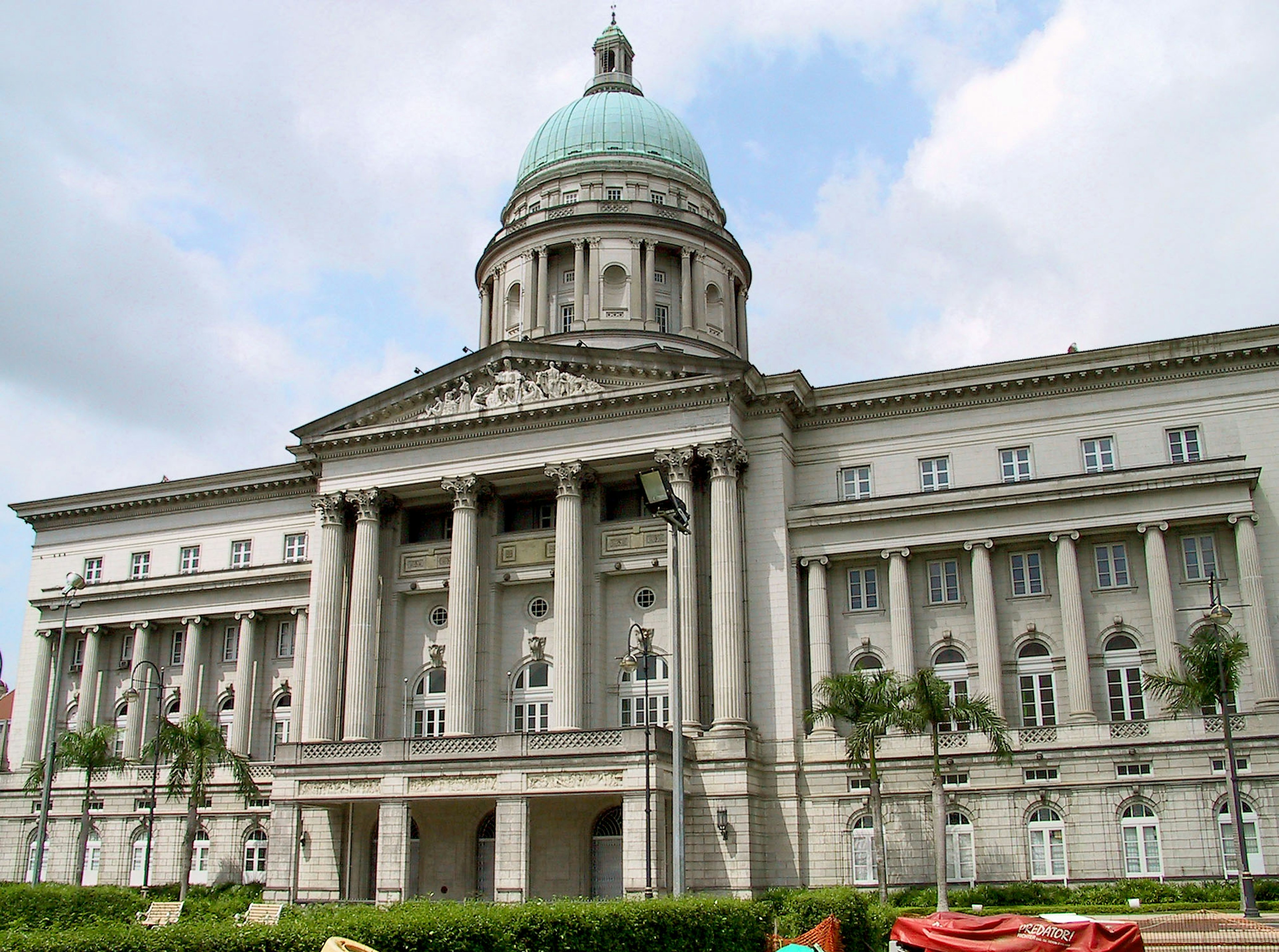 Tampilan luar Balai Kota bersejarah di Singapura dengan langit biru dan tanaman hijau di latar belakang