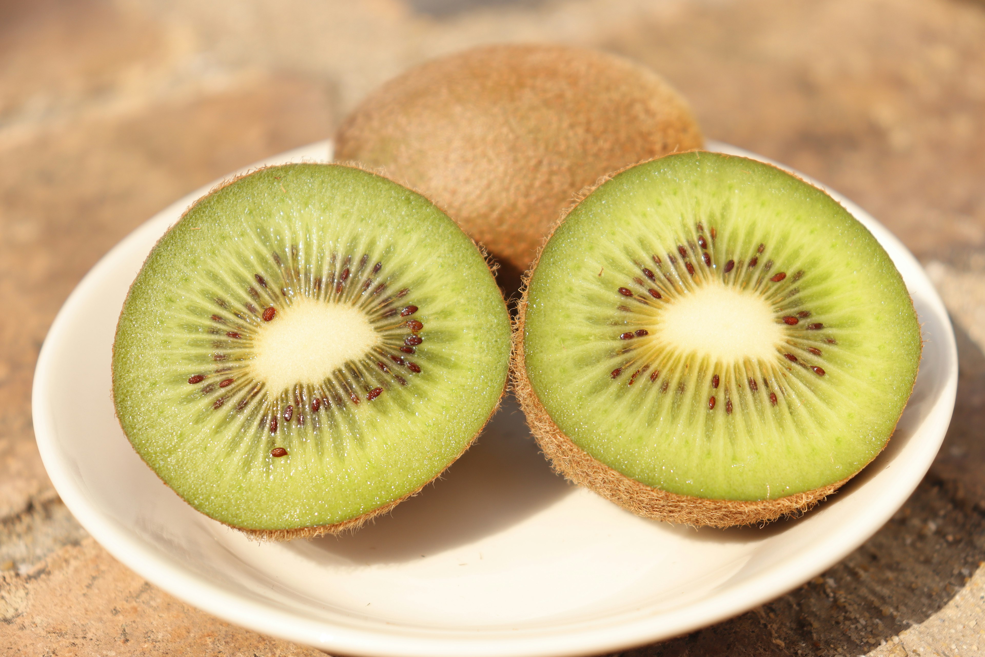 Sliced kiwi fruit on a white plate with brown background