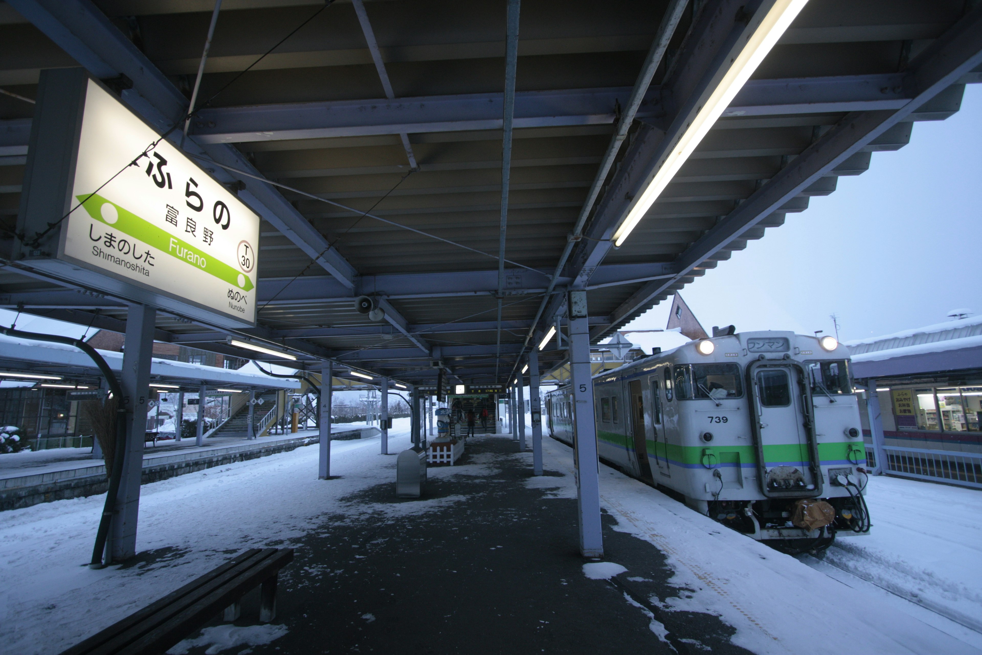 雪の降る駅に停車中の列車と駅の看板