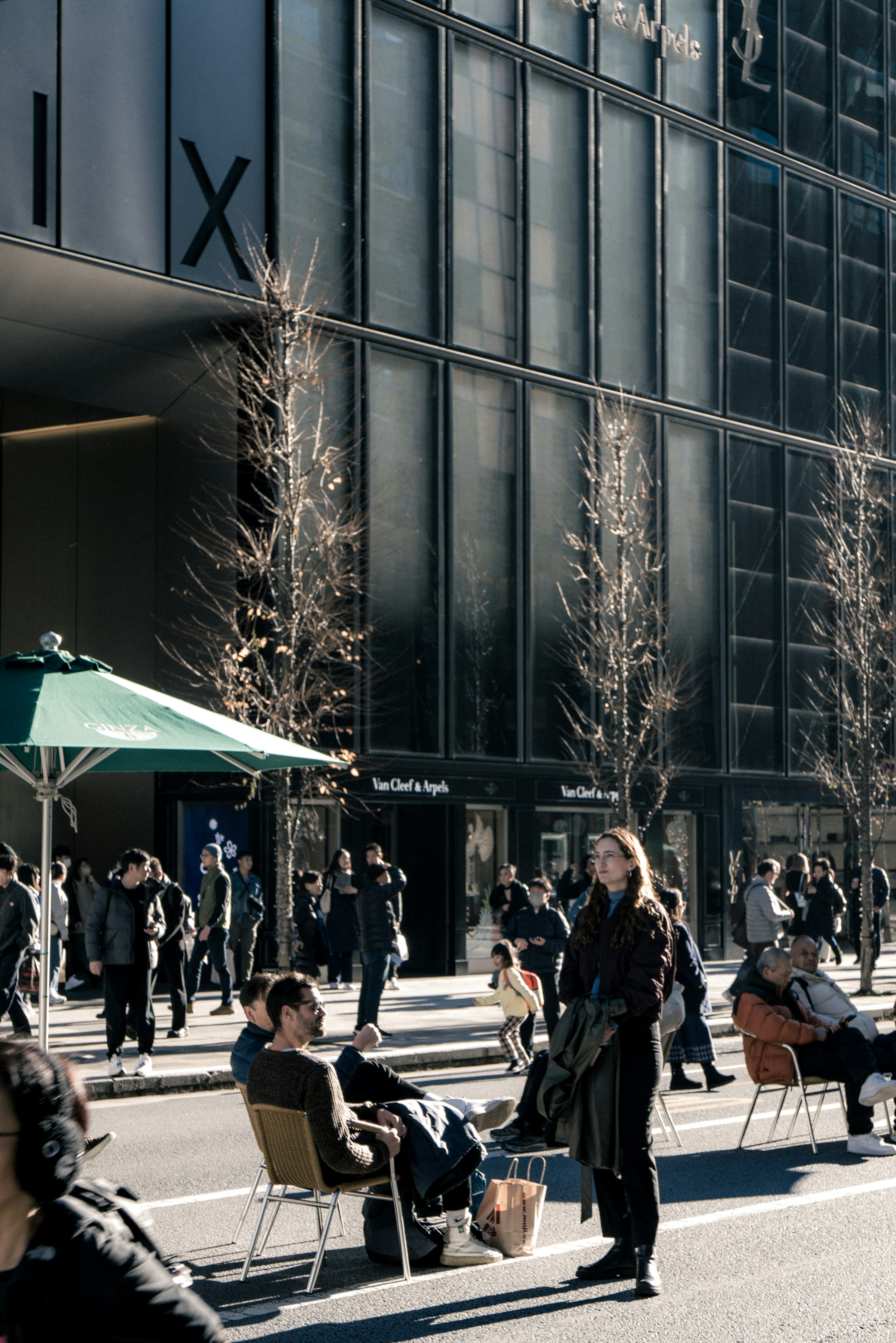 People gathering on a city street corner with men and women sitting on chairs modern building and sunlight