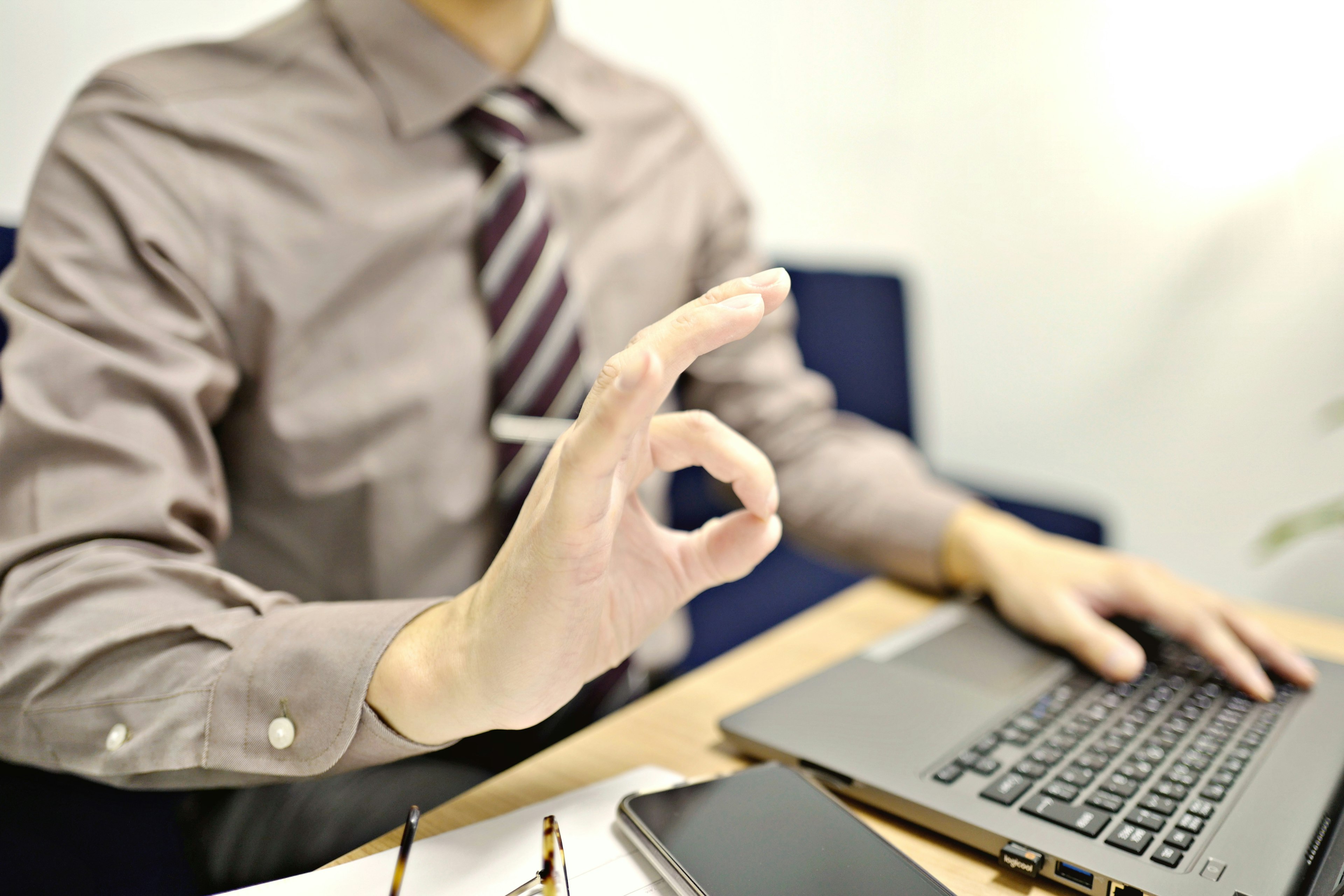 Un hombre con traje haciendo un gesto de OK frente a una computadora portátil