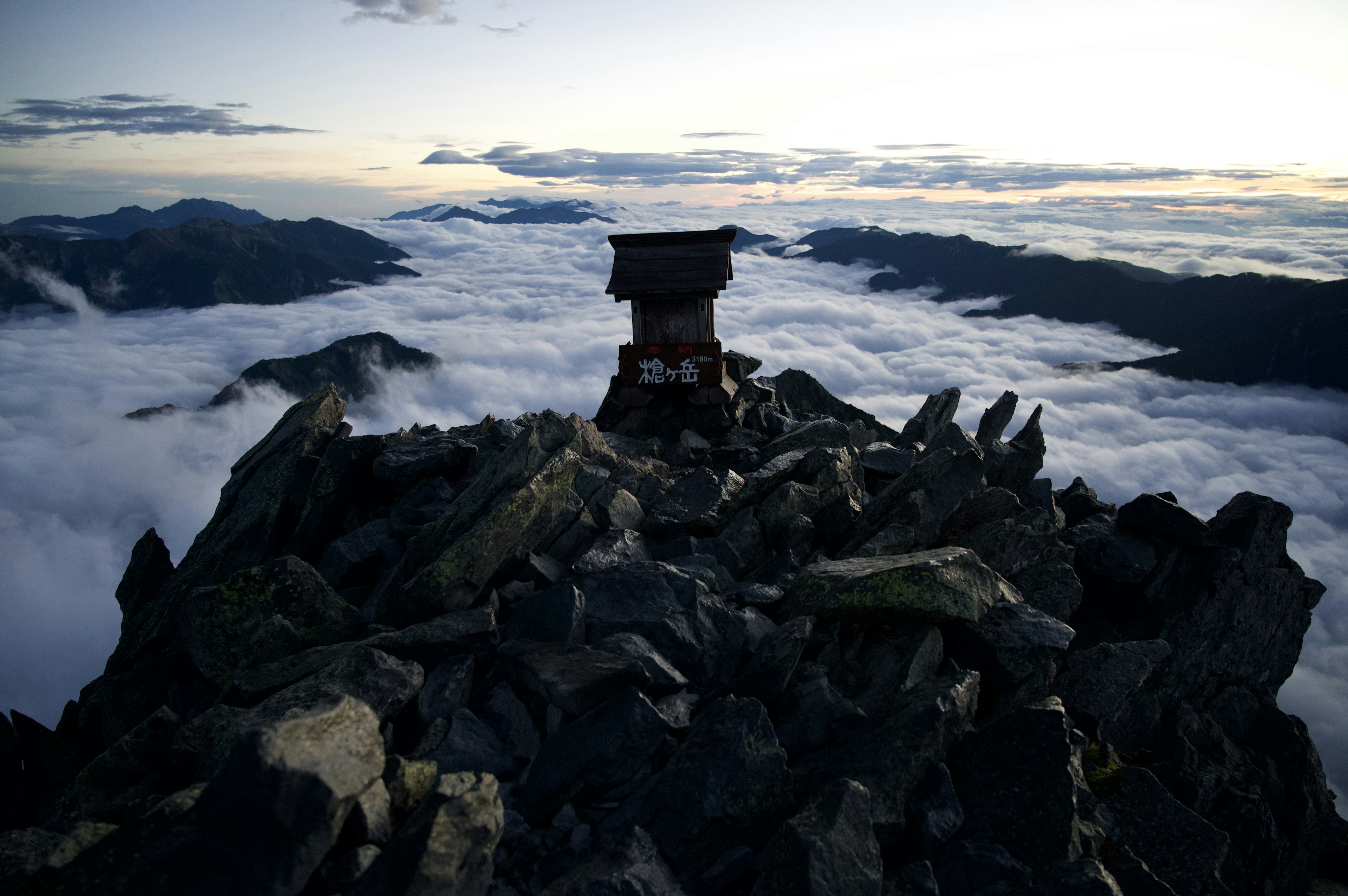 雲海の上に立つ山頂の小屋と岩石の風景