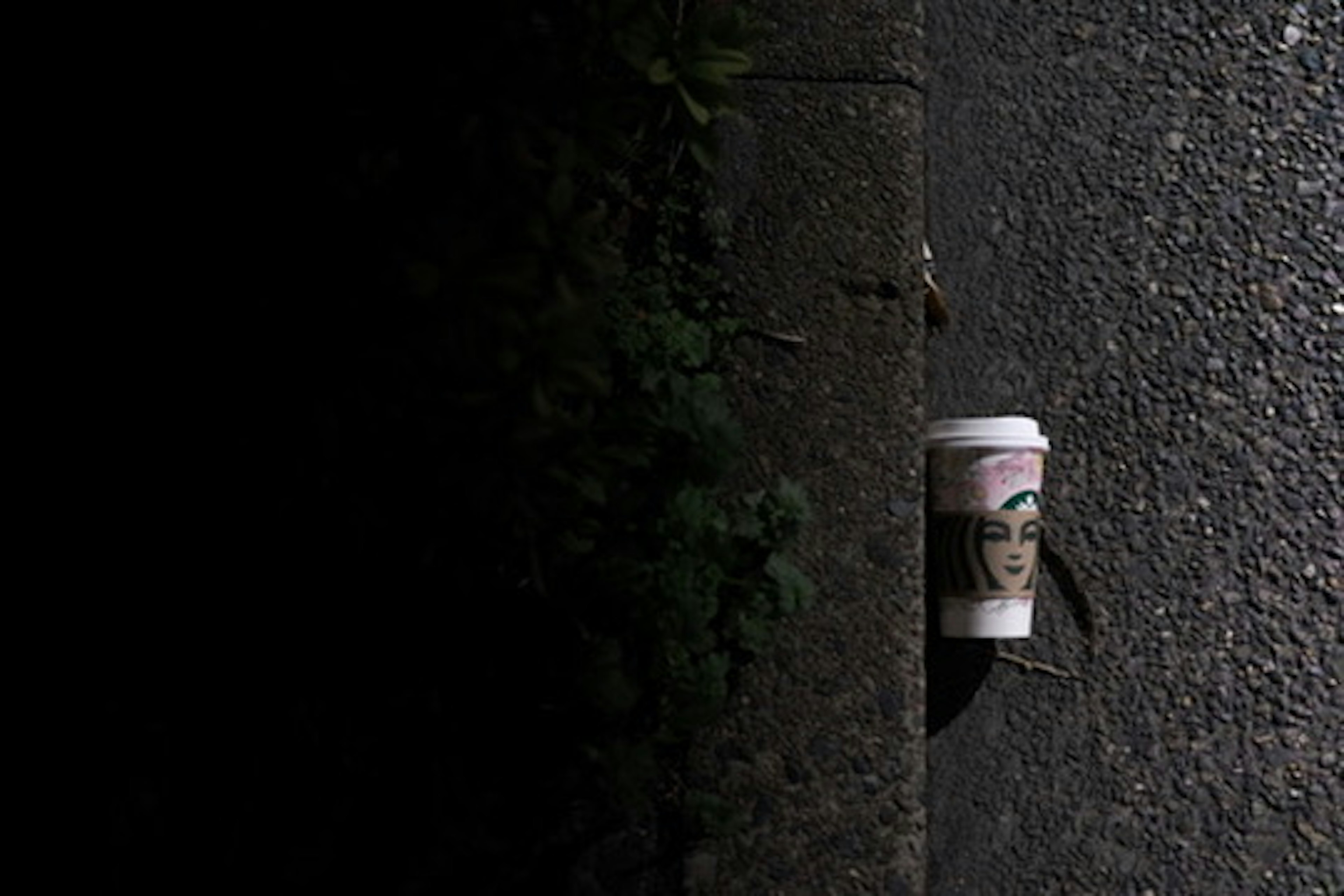 Taza de café con diseño de rostro femenino colocada en el borde de una calle oscura