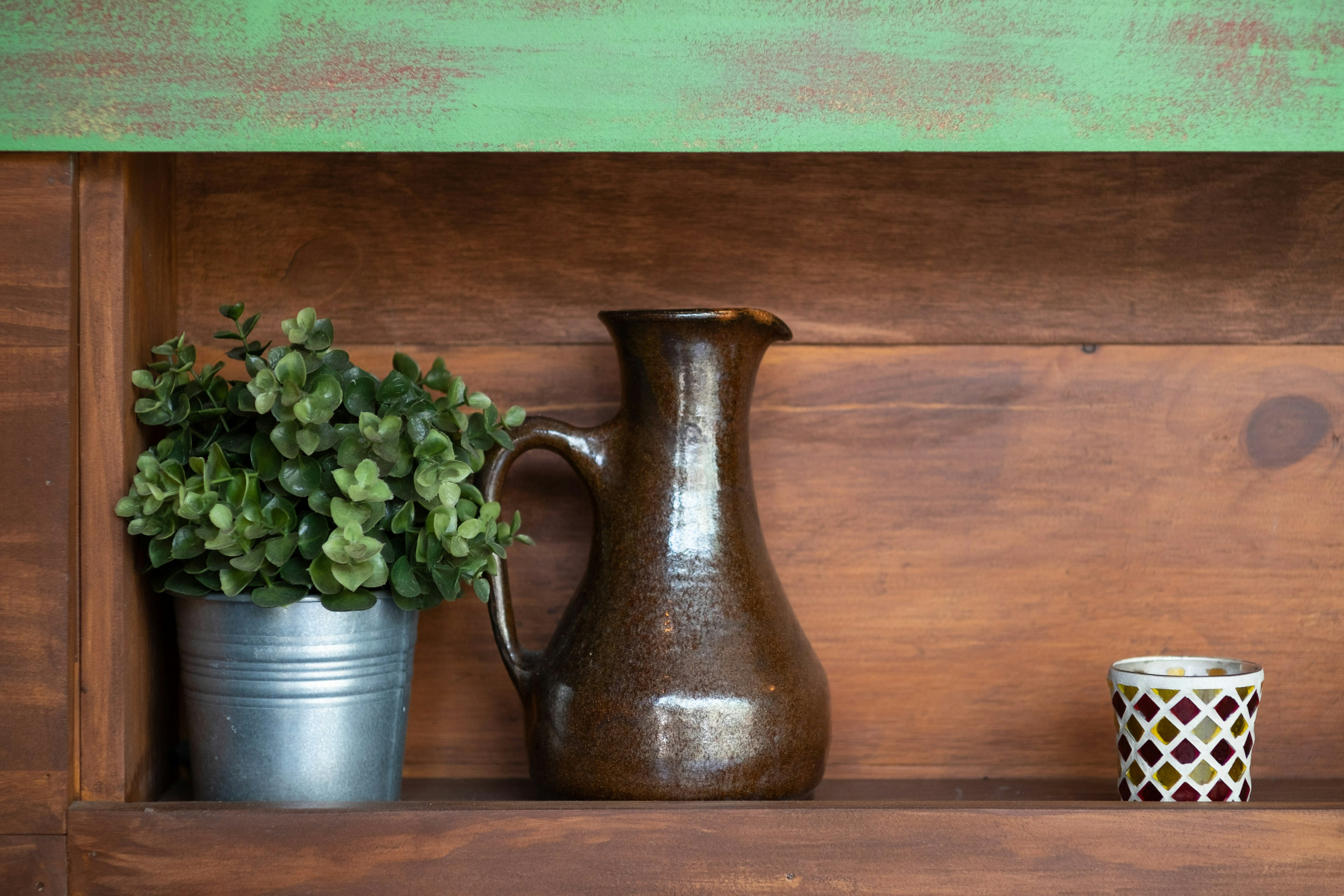 A brown ceramic pitcher and a potted plant on a green shelf