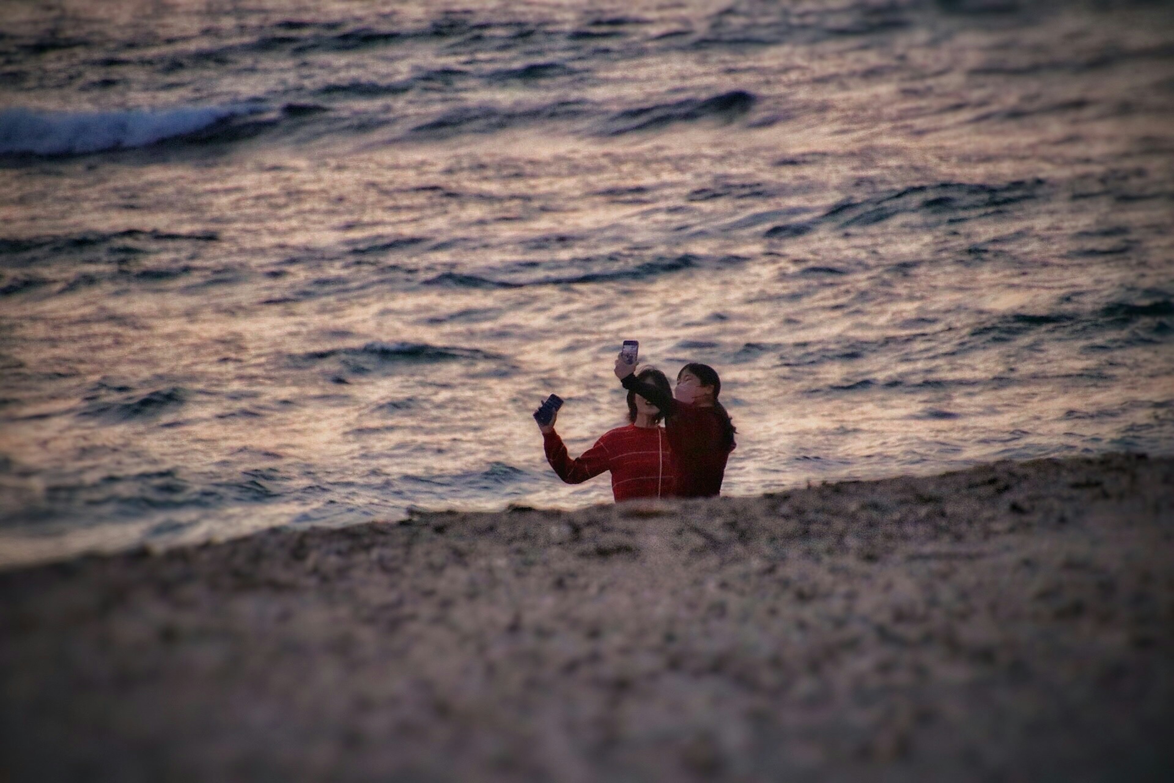 Due persone che scattano una foto sulla spiaggia vestite di rosso al tramonto