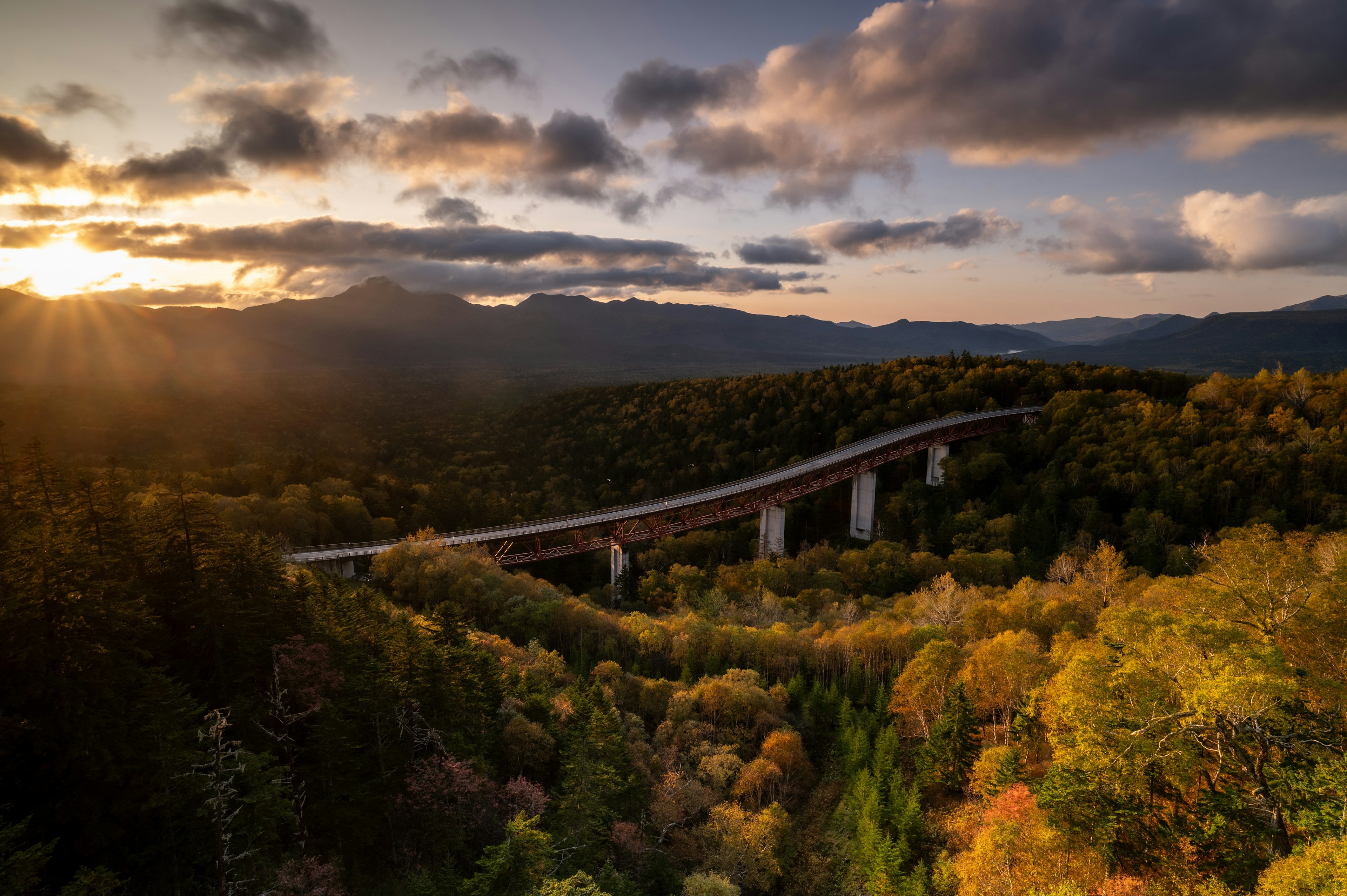 Eine Brücke, die üppige Herbstbäume mit Bergen im Hintergrund überspannt