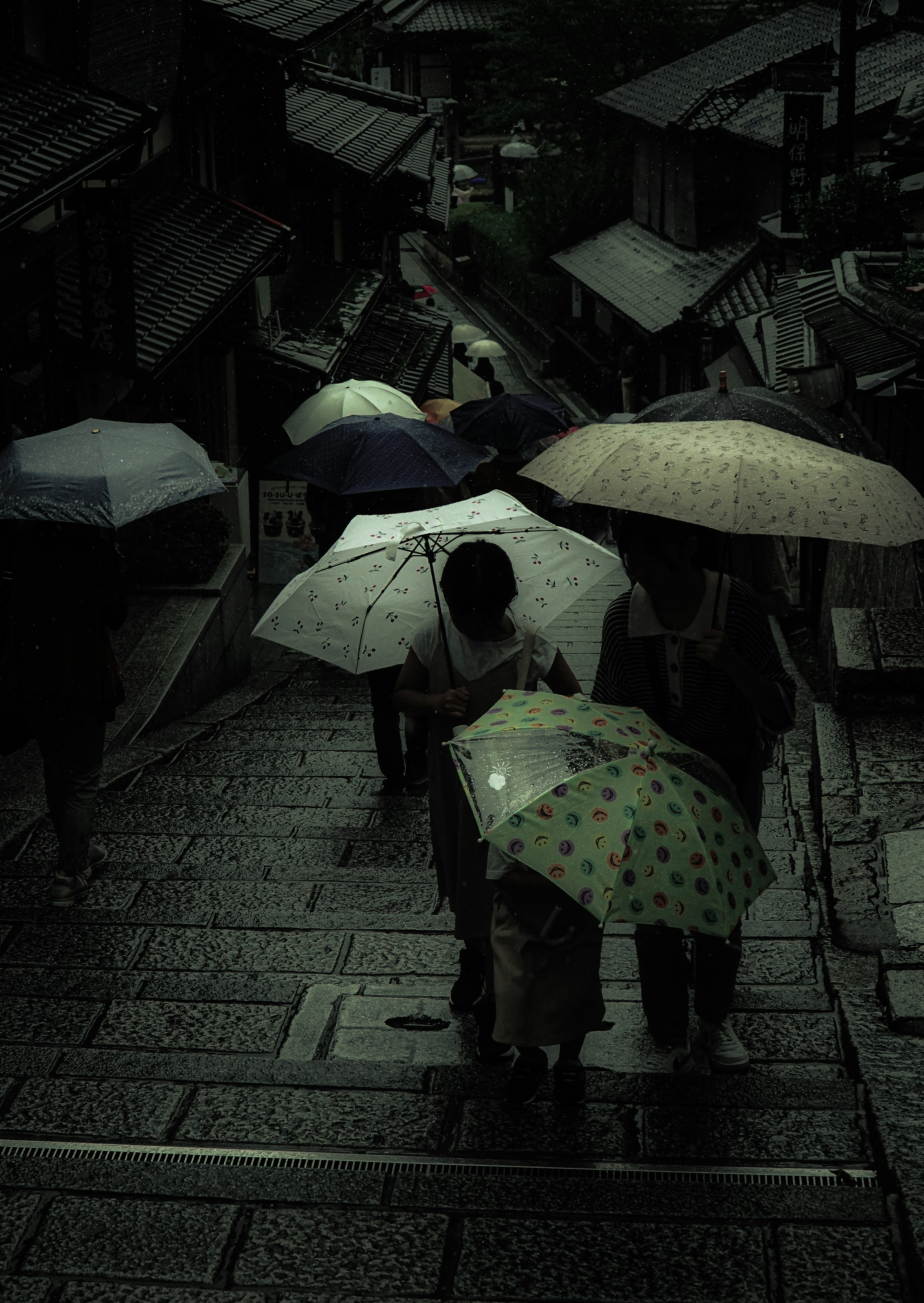 傘をさした人々が階段を下りる風景 暗い雰囲気の京都の街並み