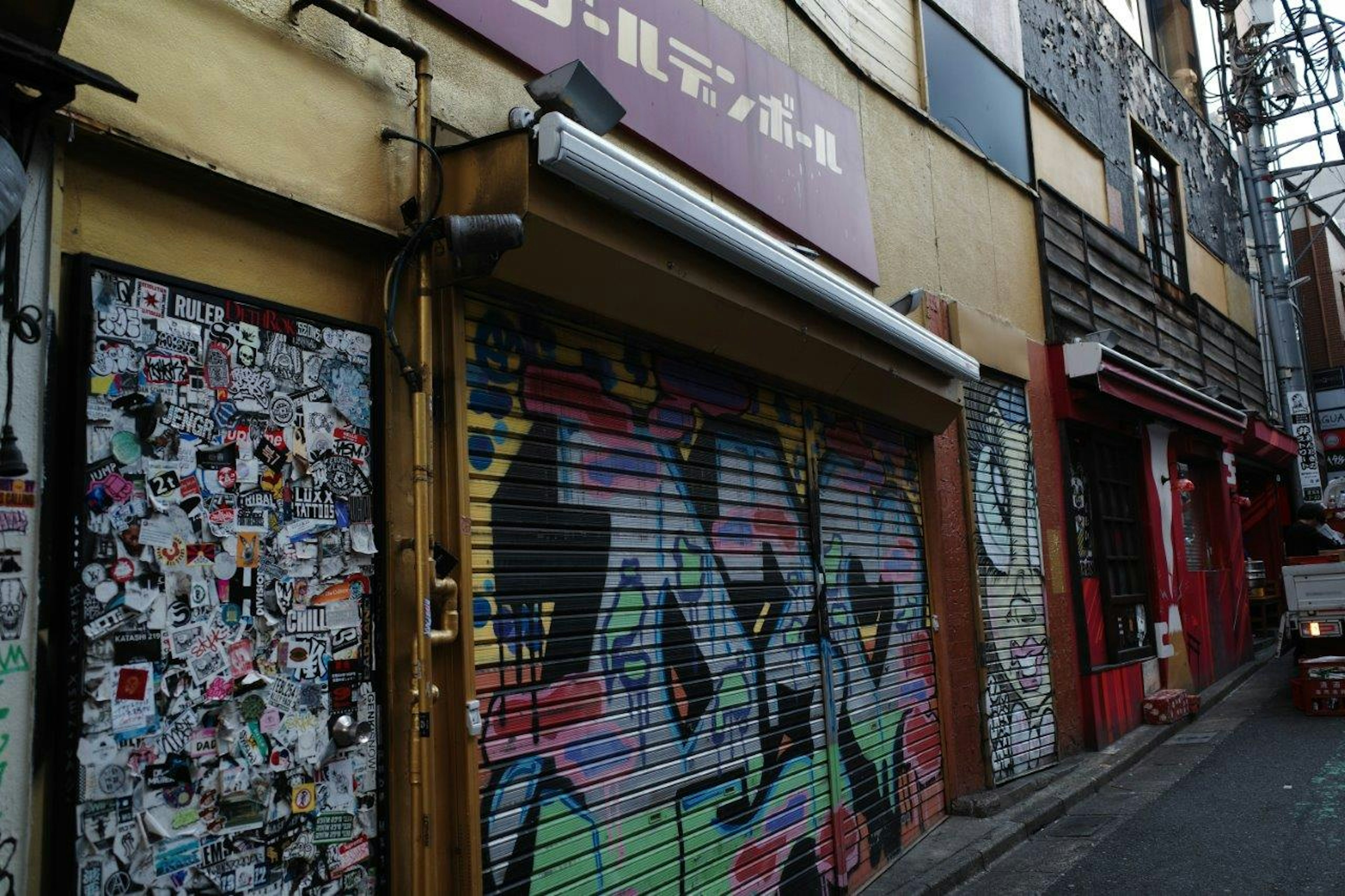 Allée étroite avec un rideau de fer recouvert de graffiti colorés et des murs ornés d'autocollants