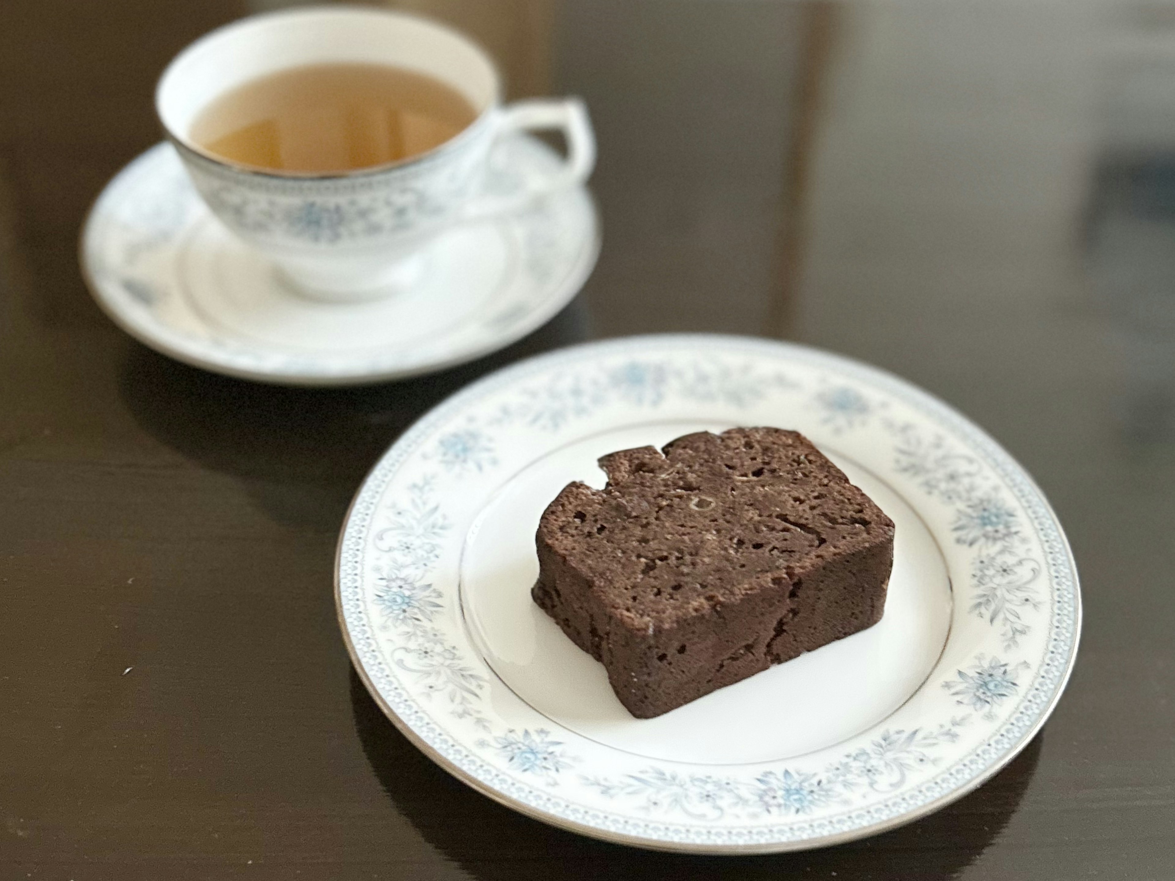 A plate with brownie and a cup of tea on a wooden table