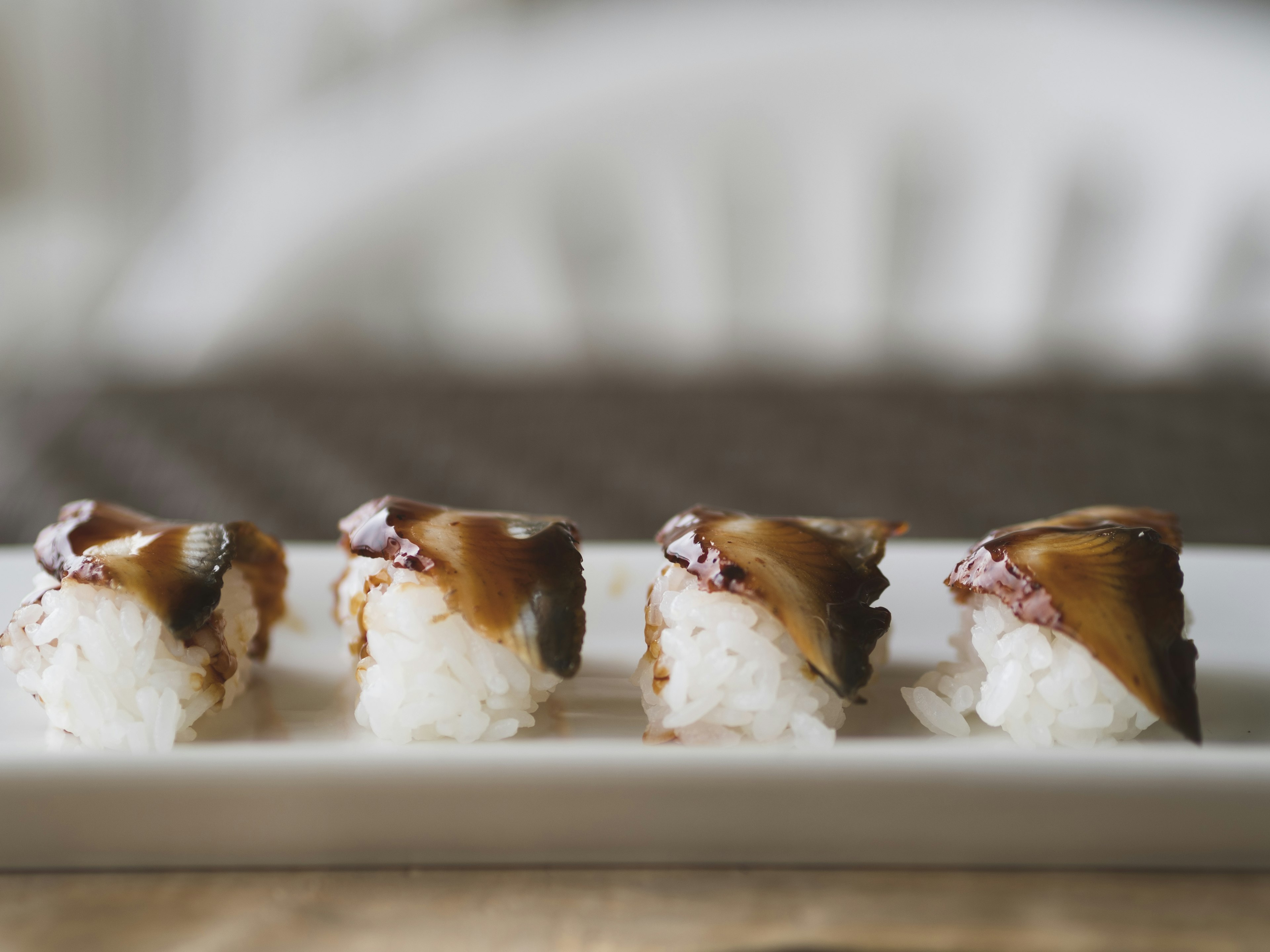 Une rangée de sushi sur une assiette blanche garnie de saumon et de sauce sucrée