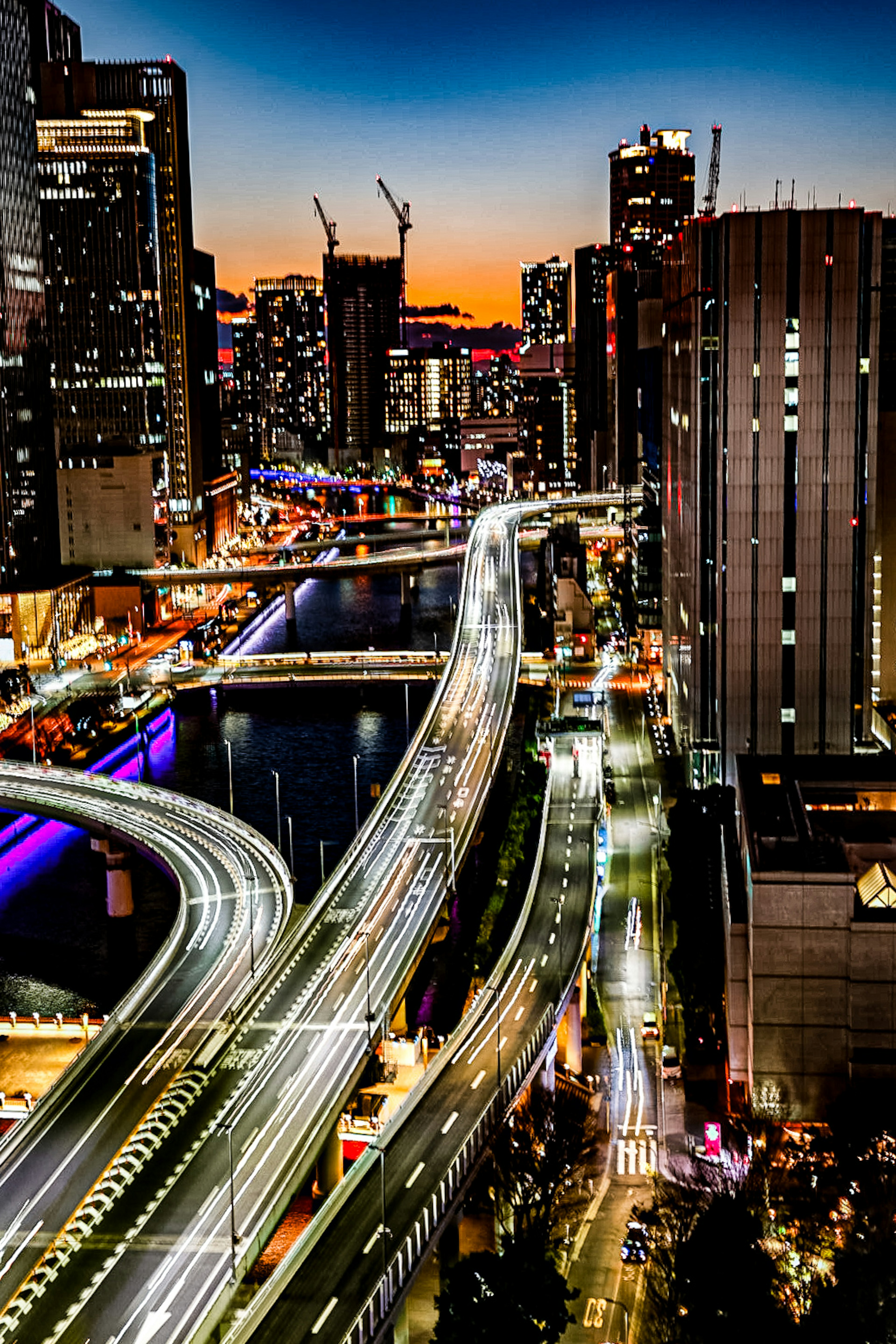 Night cityscape featuring skyscrapers and a river with flowing traffic