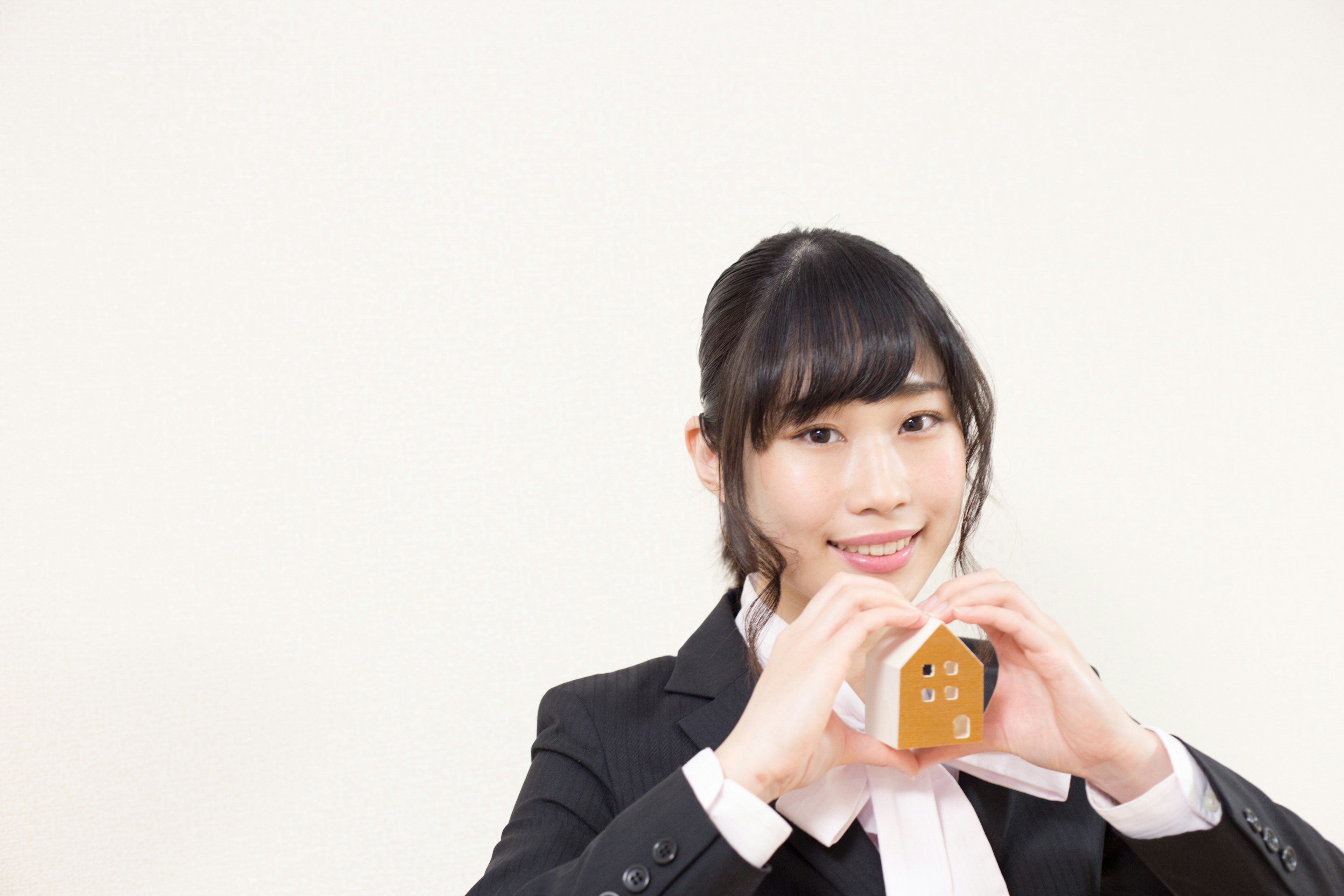 Une femme en costume souriante tenant un petit objet en forme de maison