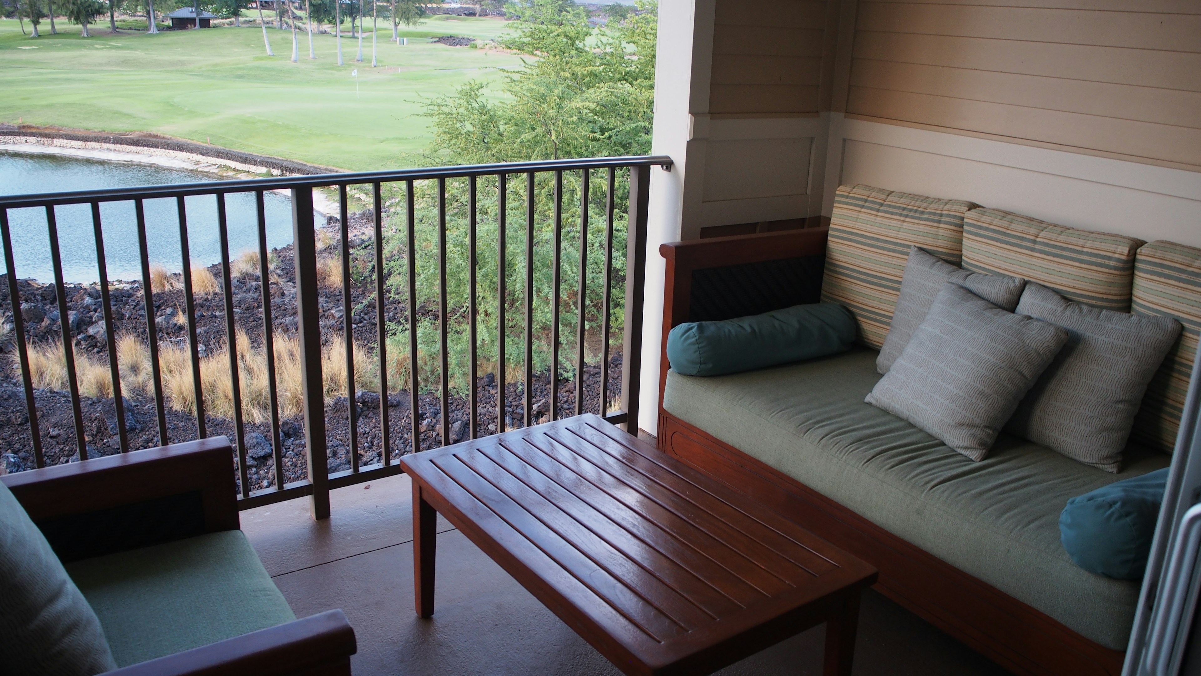 Area balkon yang nyaman dengan meja kayu dan bantal menghadap ke area hijau