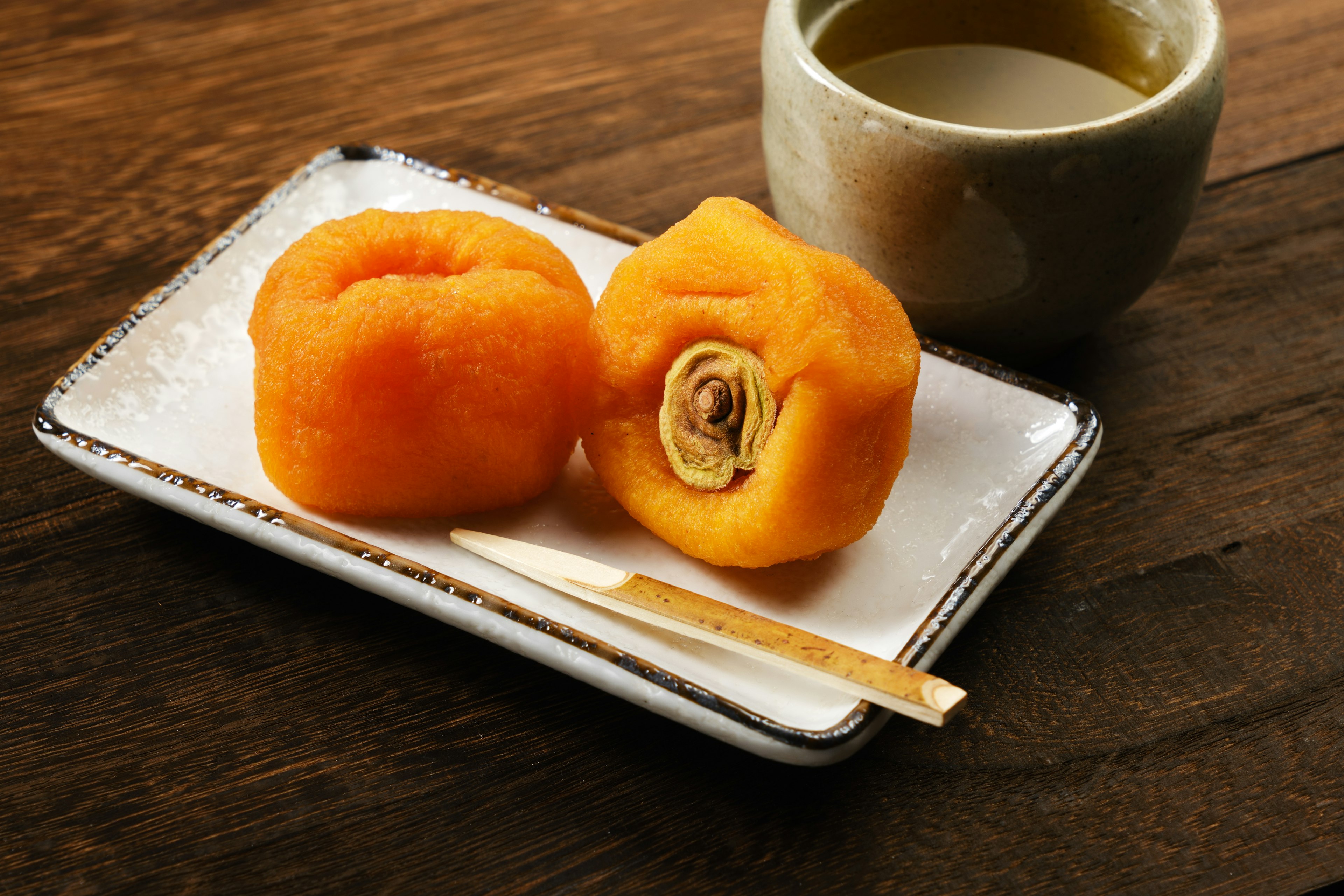 Zwei orangefarbene japanische Süßigkeiten auf einem Teller mit einer Tasse Tee