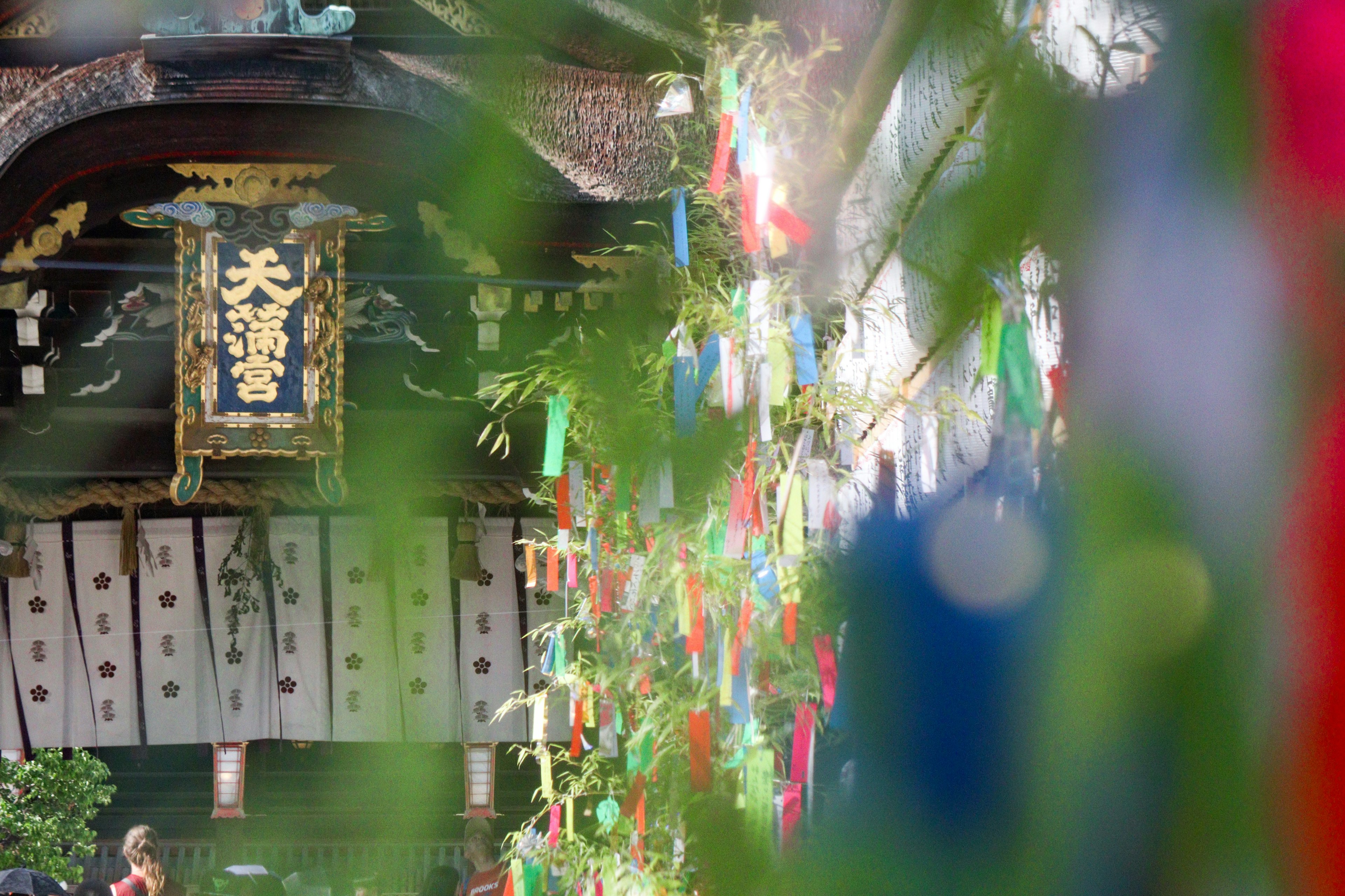 Bunte Tanzaku hängen von Bambusblättern mit einem traditionellen japanischen Gebäude im Hintergrund