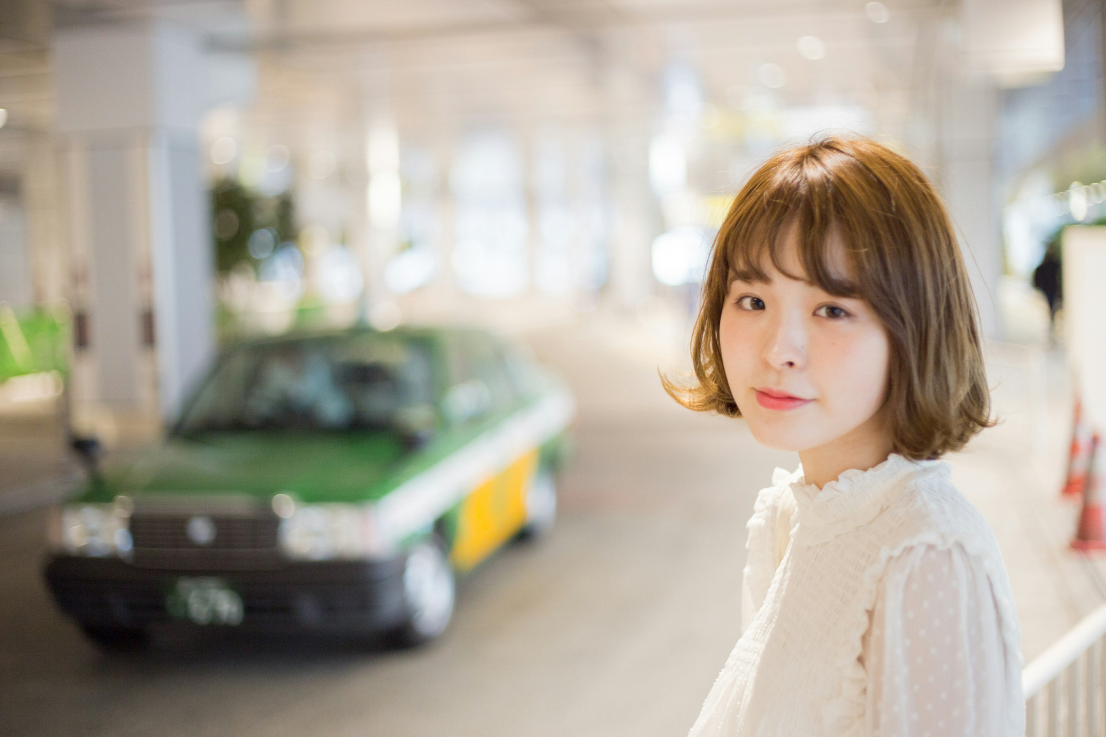 A woman with short hair standing in a bright background with a green taxi