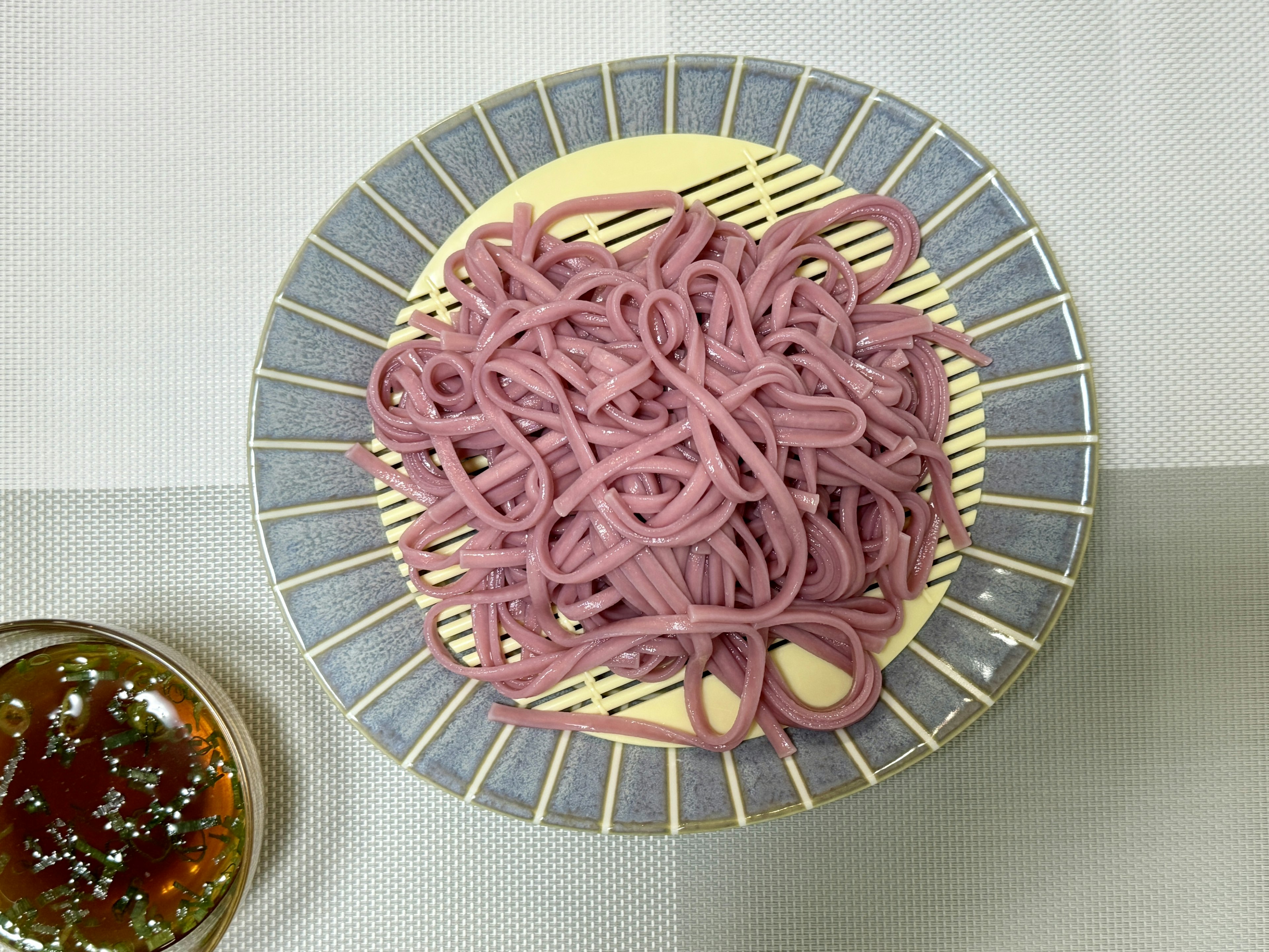 Un plato de fideos morados y un tazón de salsa