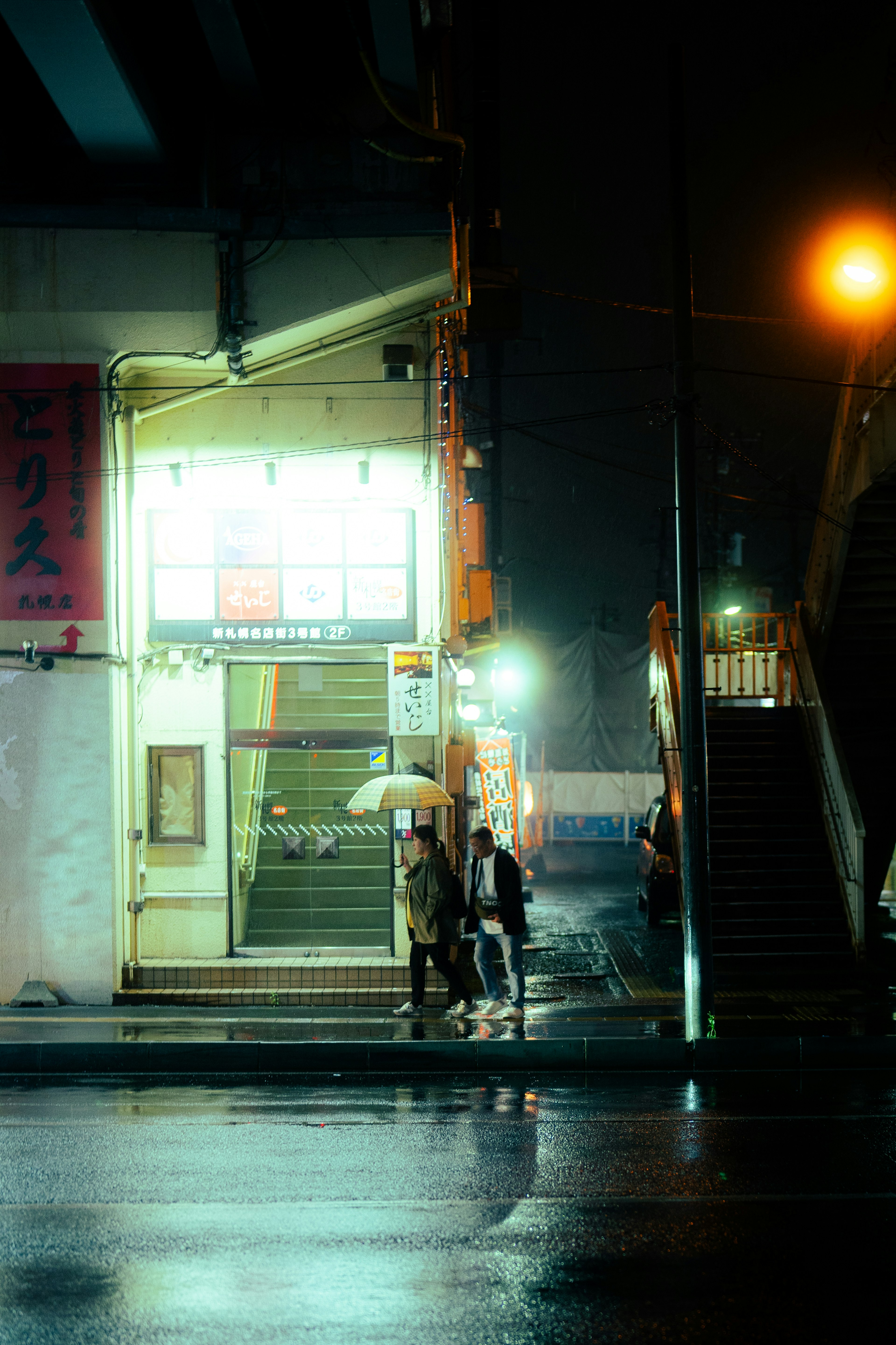 Night street scene with people holding umbrellas near stairs in the rain