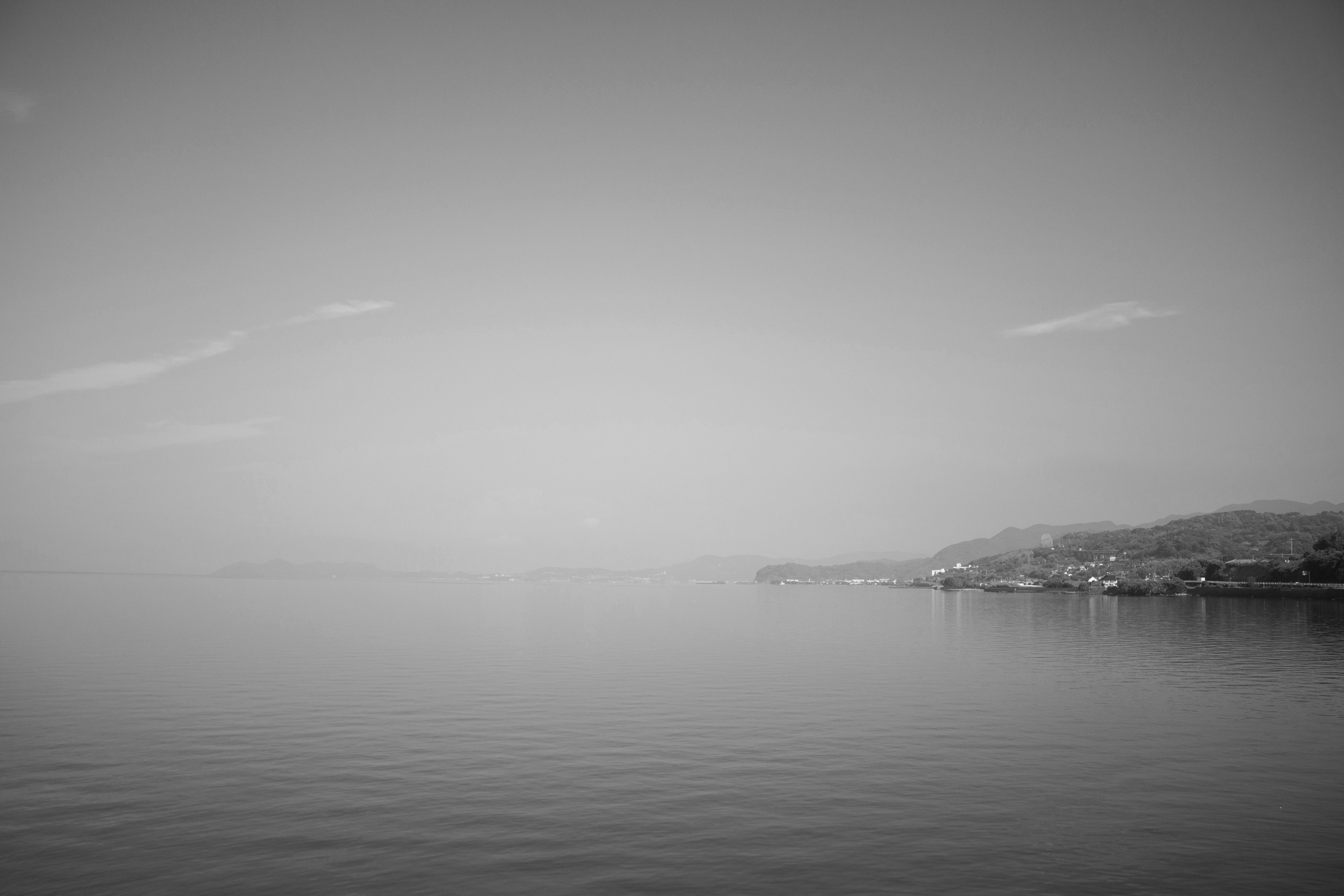 Paesaggio in bianco e nero di mare e cielo superficie d'acqua calma e colline lontane