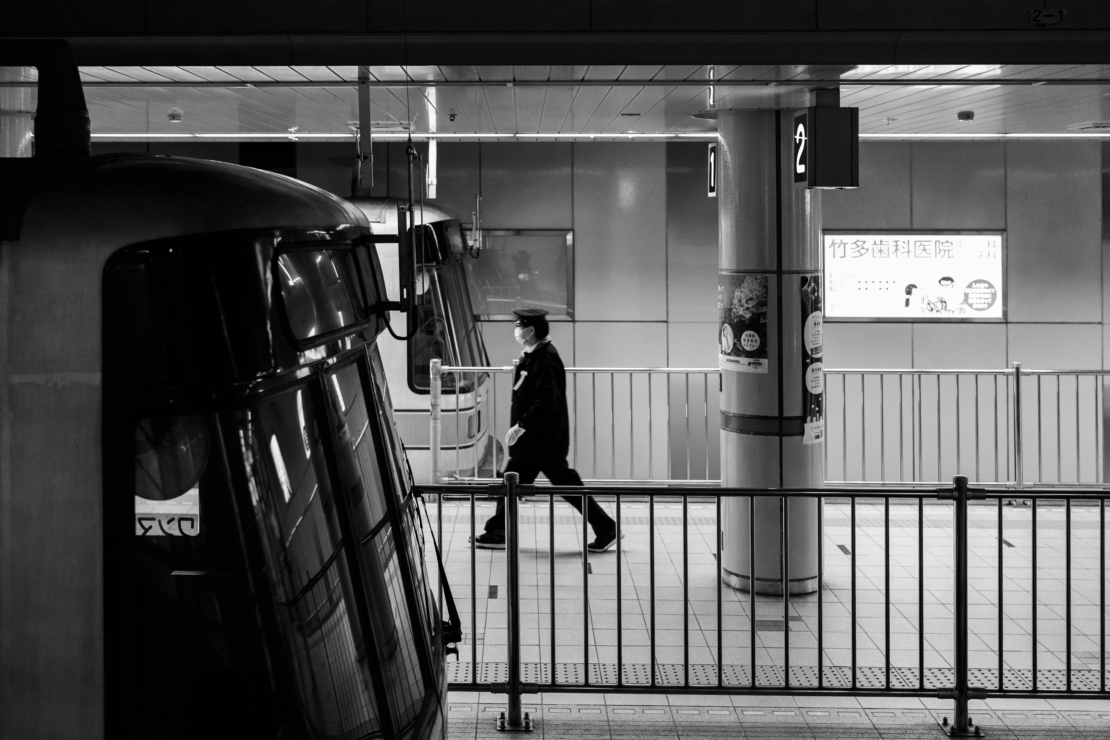 Escena de estación en blanco y negro con una persona caminando y un tren en primer plano