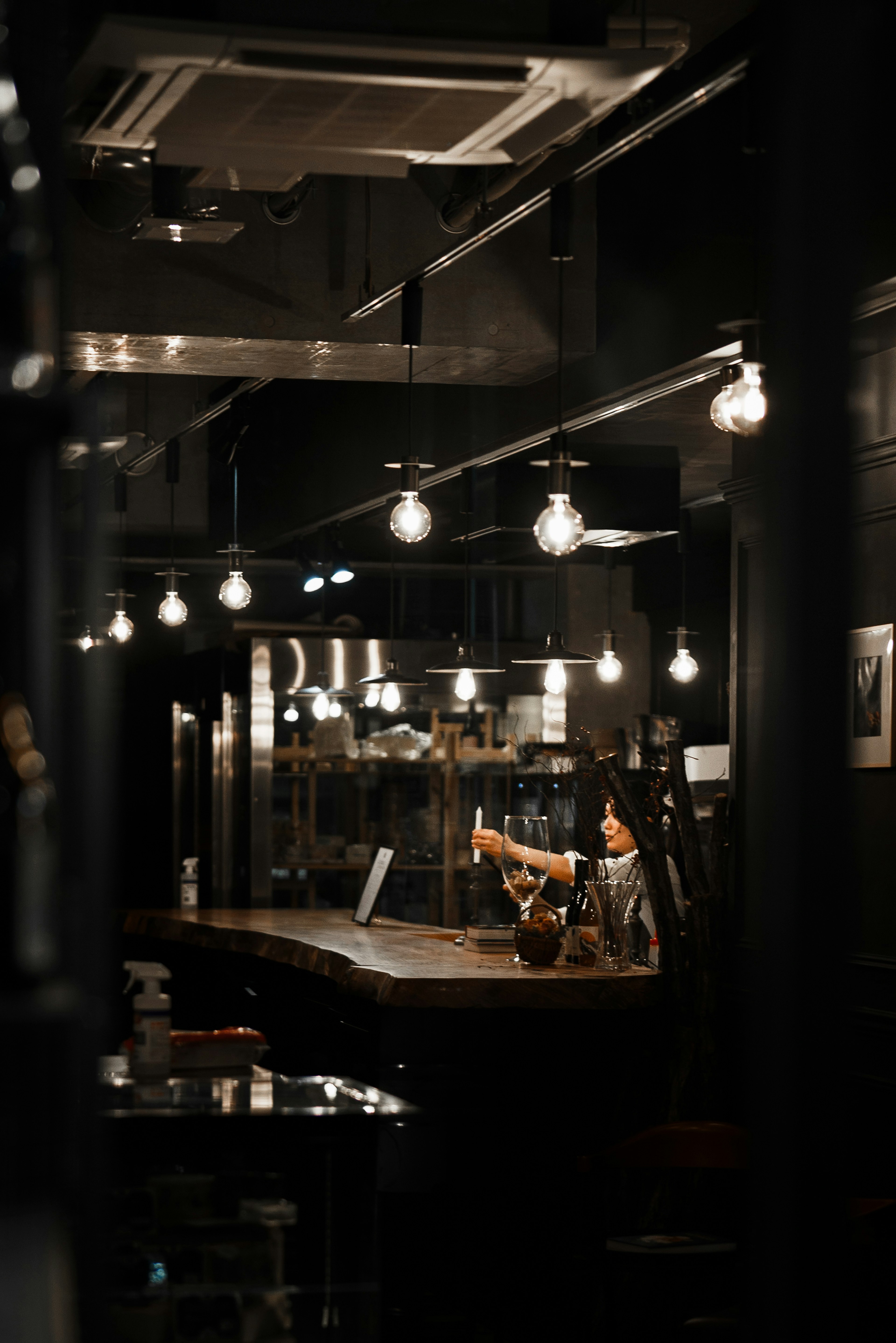 Interno di un bar poco illuminato con un barista al bancone e luci sospese