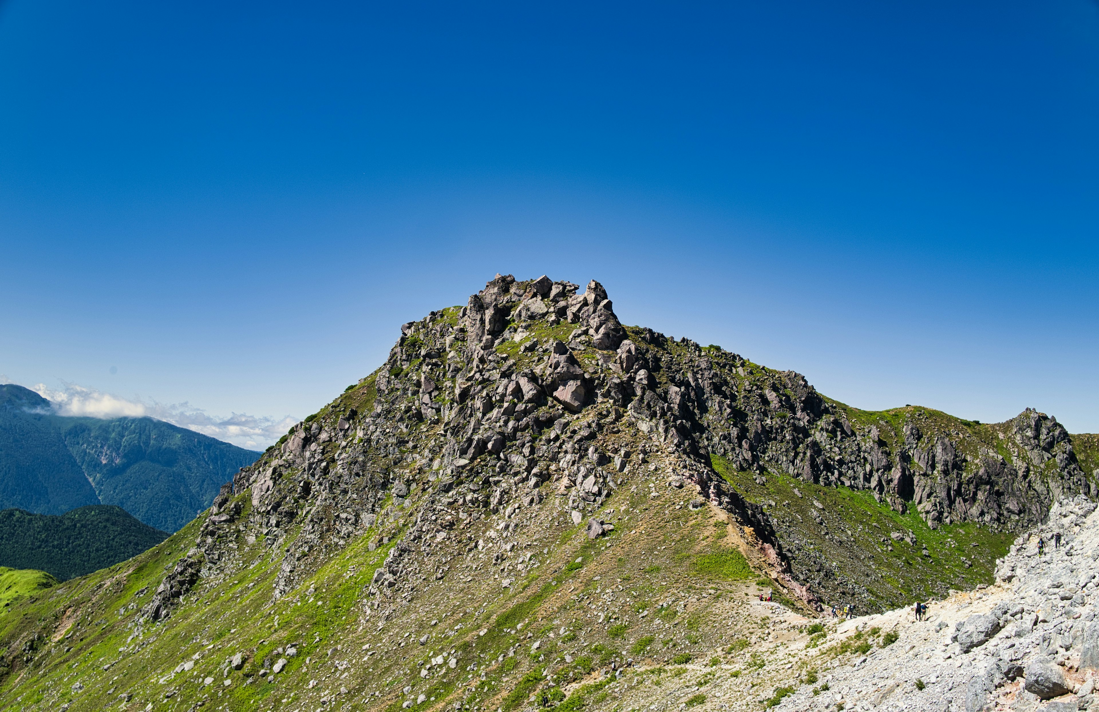 Rocky mountain landscape under a clear blue sky featuring lush green grass