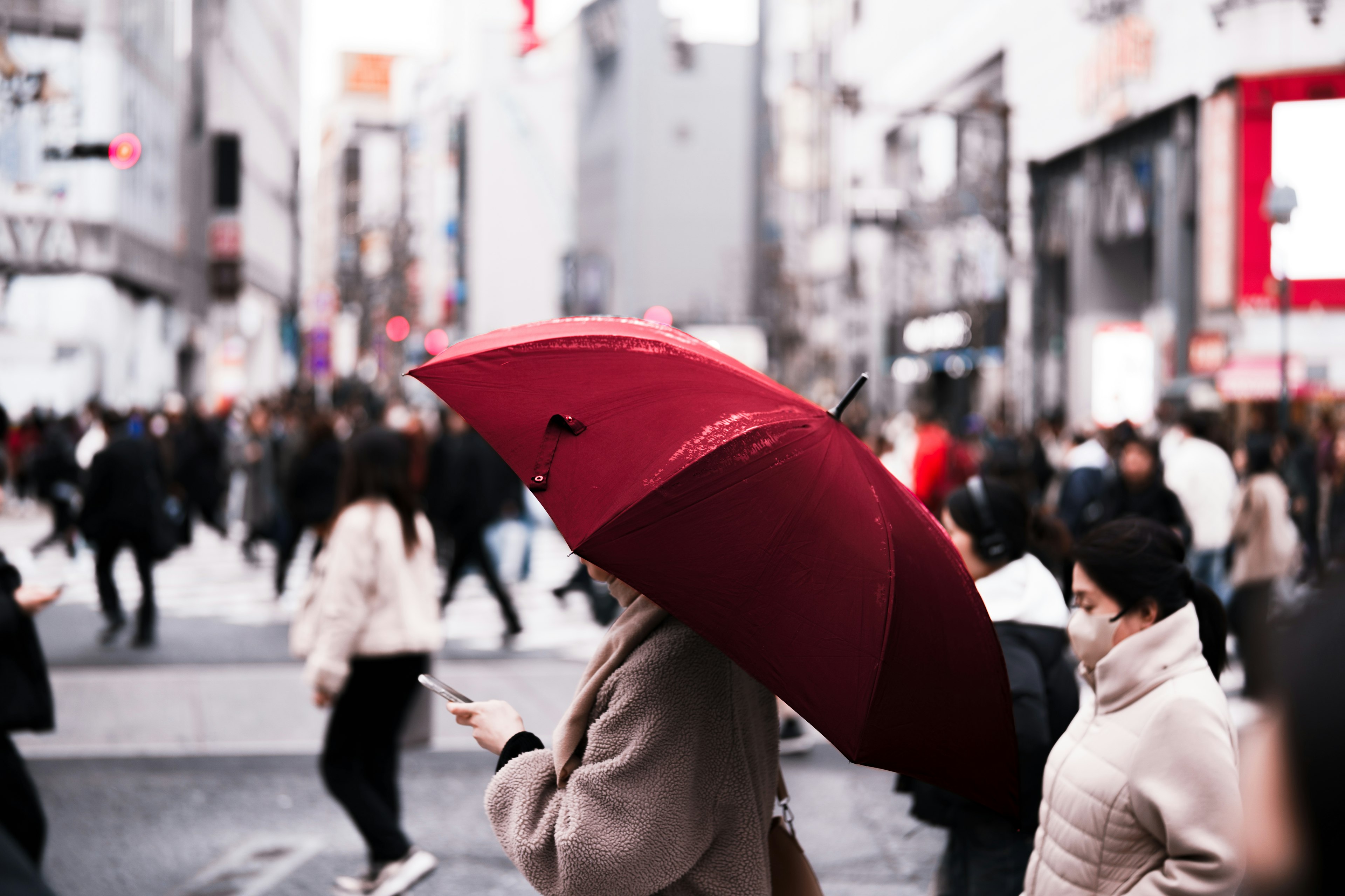 人混みの中で赤い傘を持つ女性が歩いている