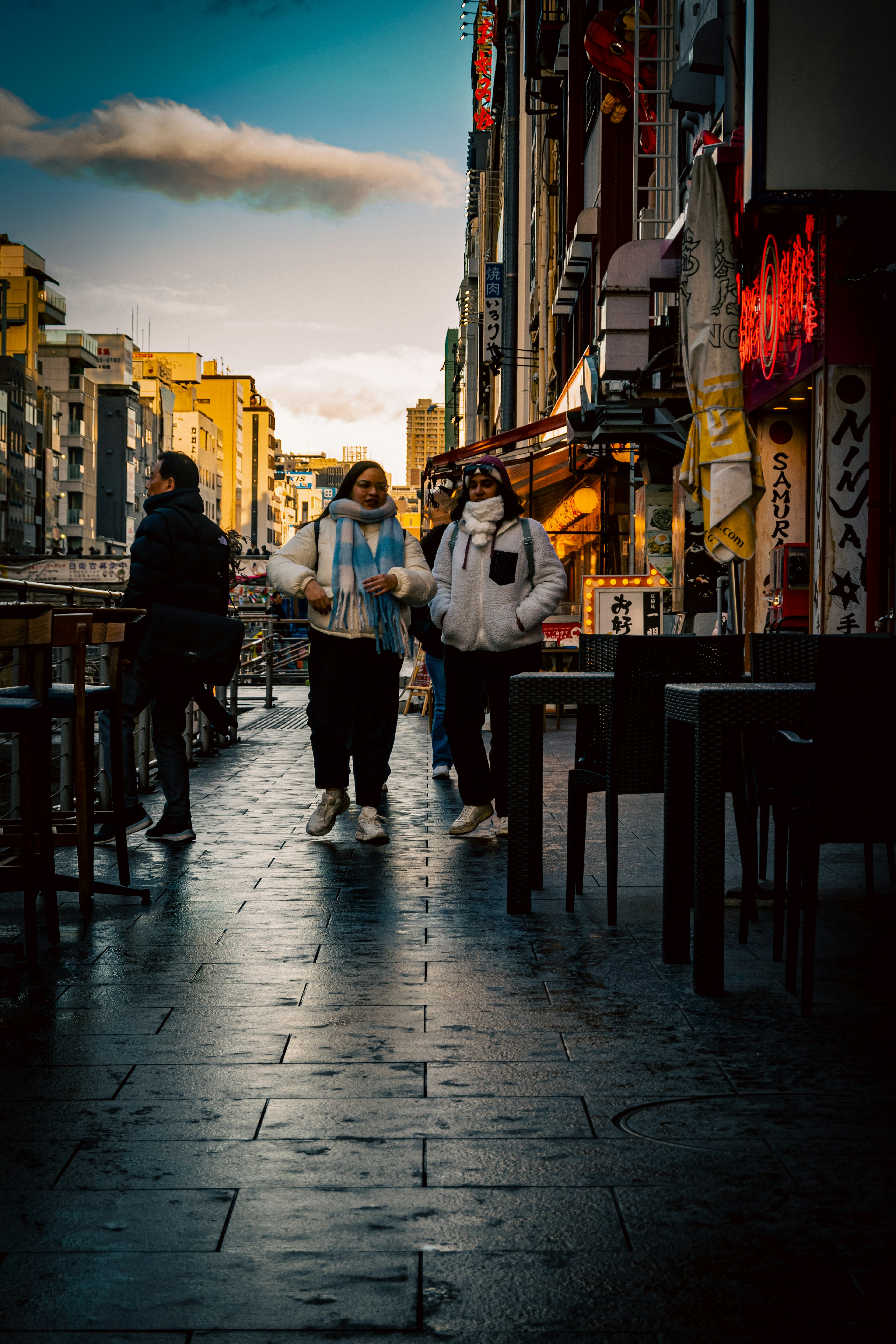 Two people walking in an urban setting during twilight with other pedestrians