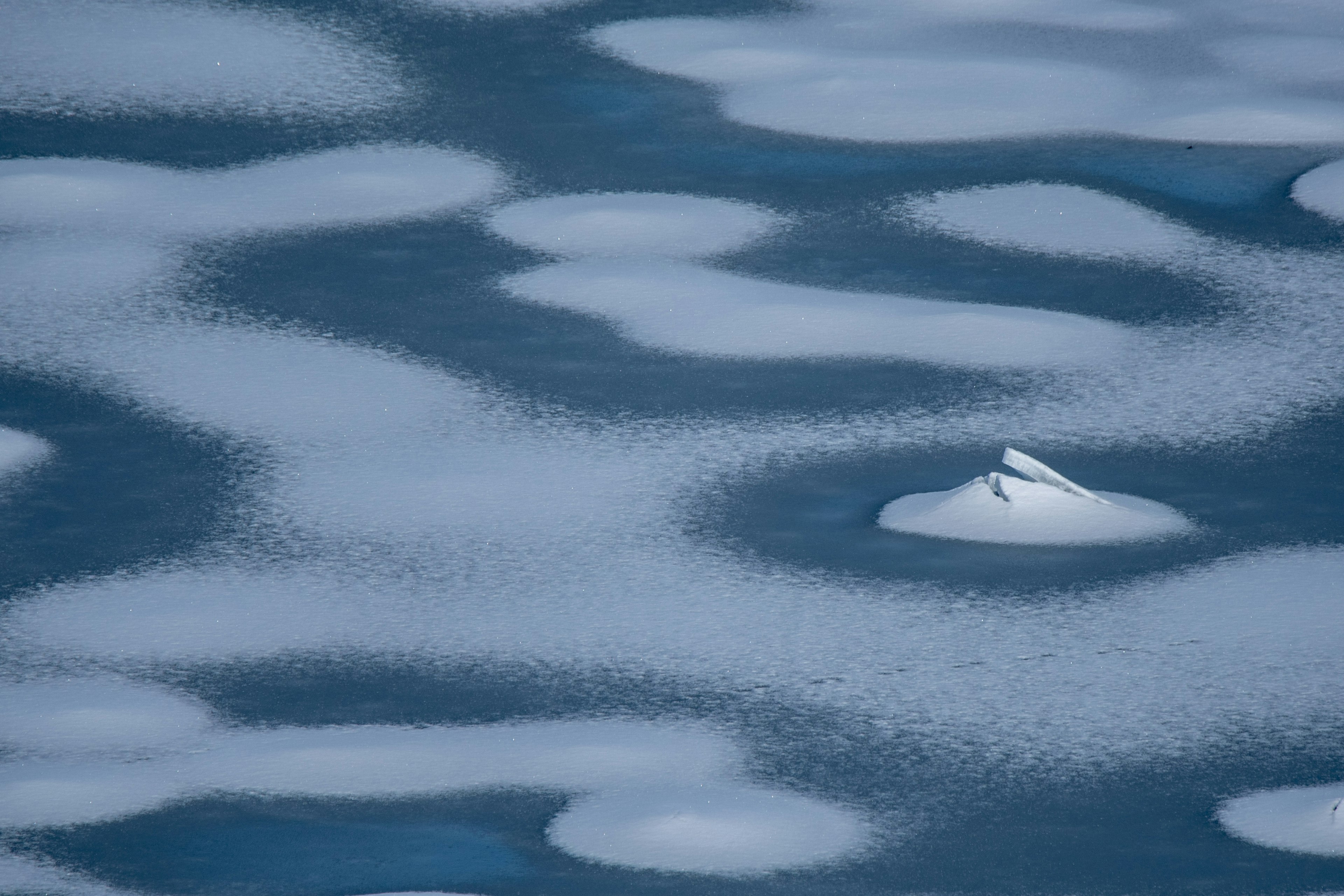 Patterns of snow on a cold blue water surface with ice formations