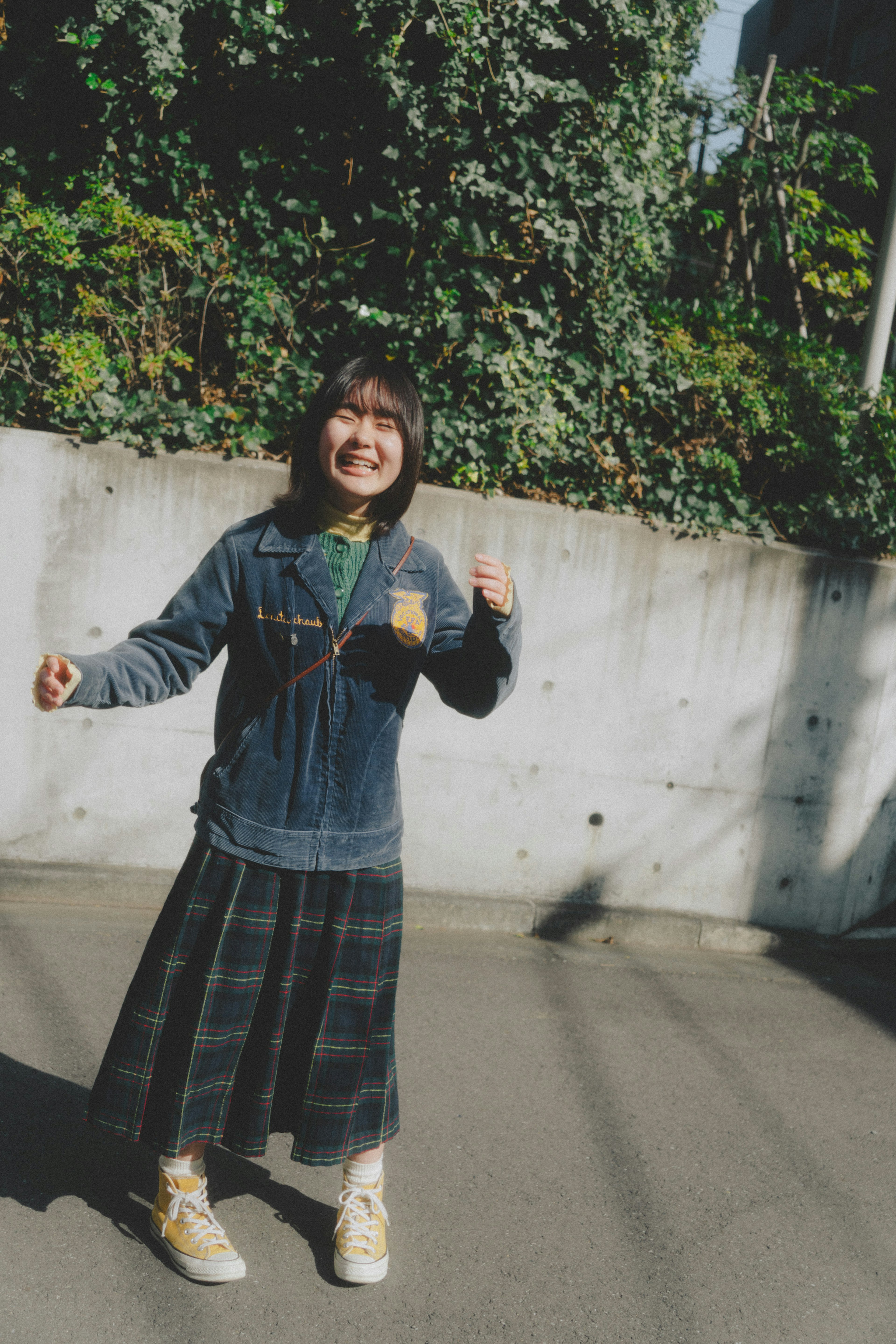 Smiling woman posing in denim jacket and plaid skirt with green background