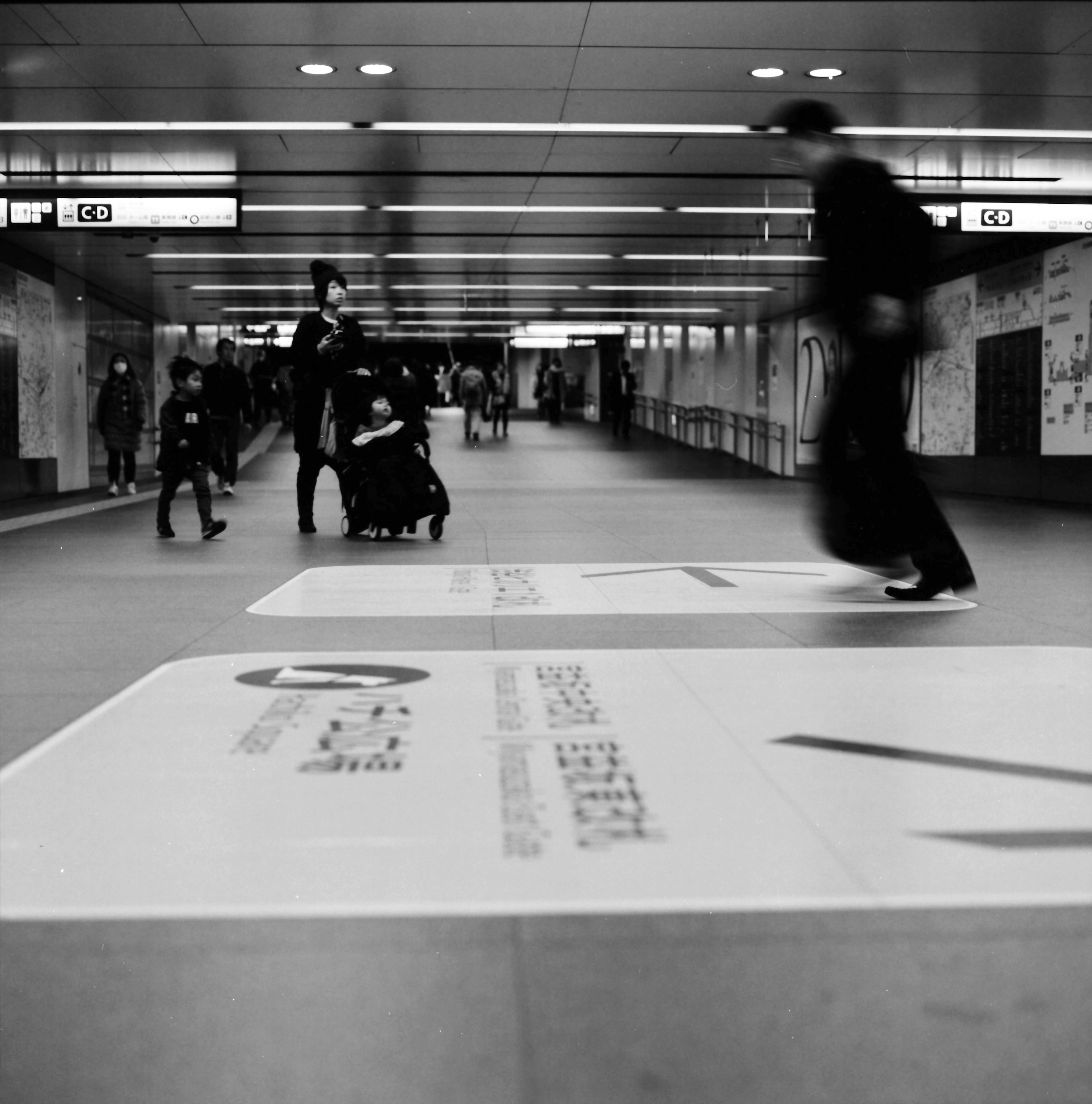 Passage piéton animé dans une station de métro avec des personnes en mouvement et des publicités en noir et blanc